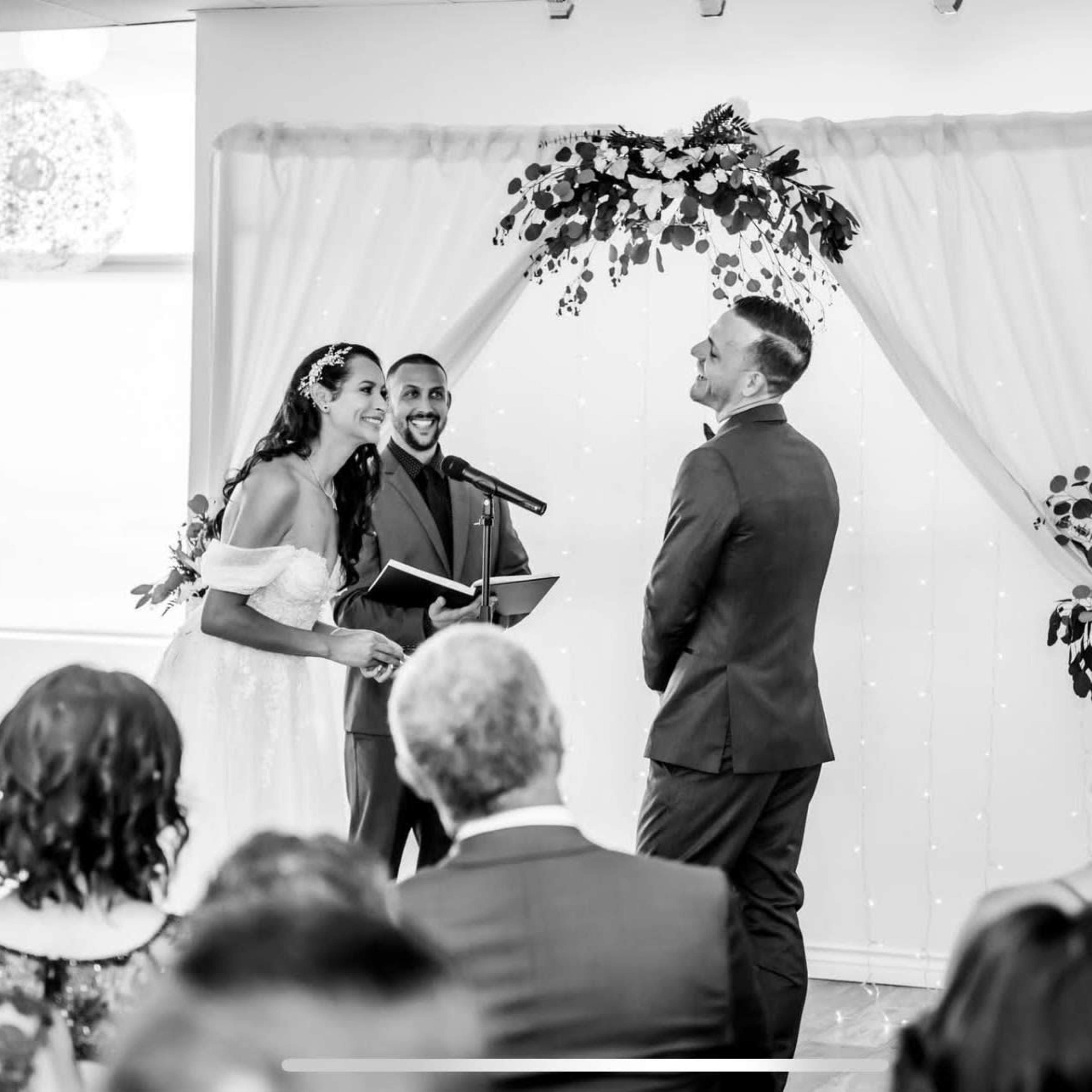 A couple stands at an altar decorated with greenery as they exchange vows during a wedding ceremony.