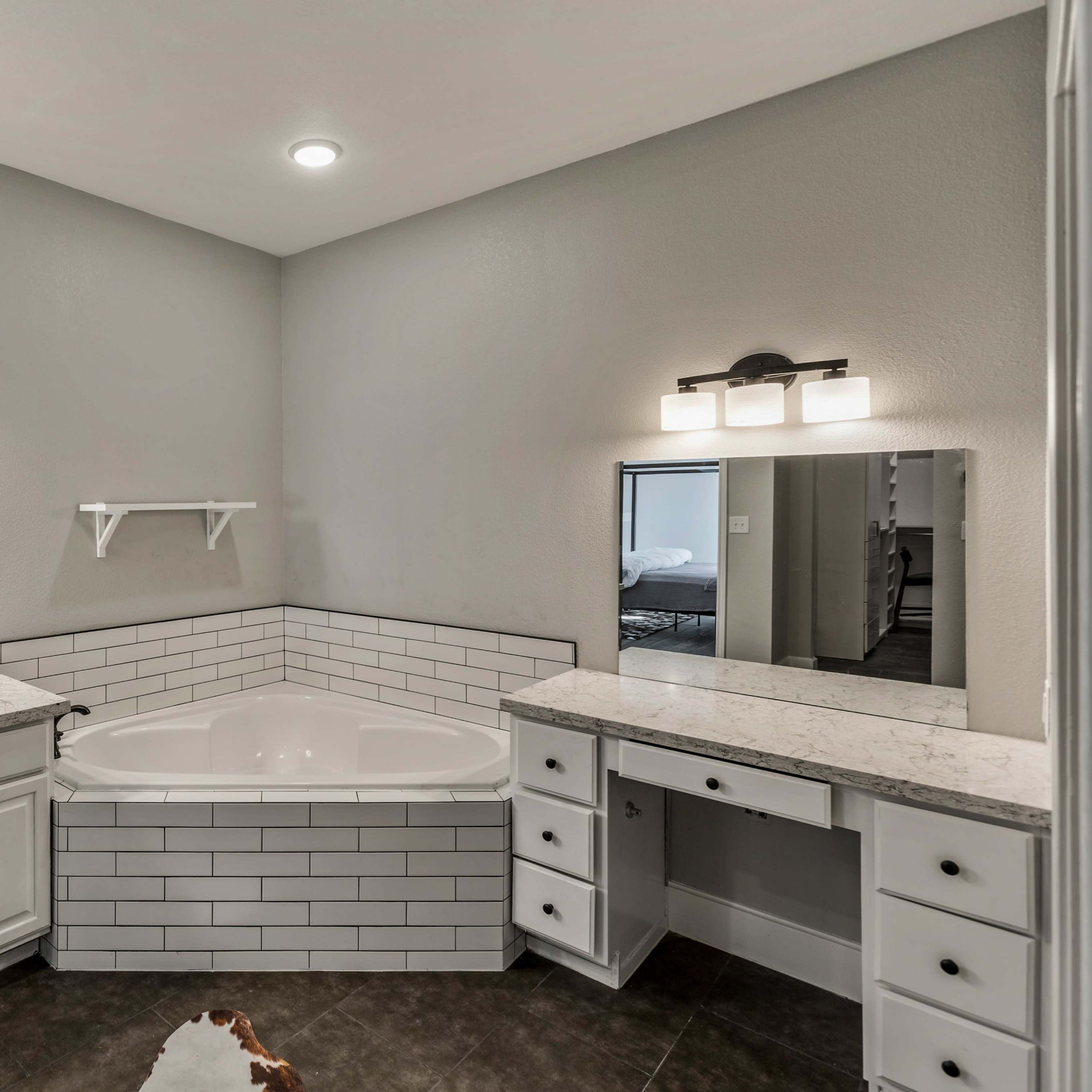 A modern bathroom with a large soaking tub, dual sinks, and a spacious countertop, featuring white cabinetry and a light gray color scheme.