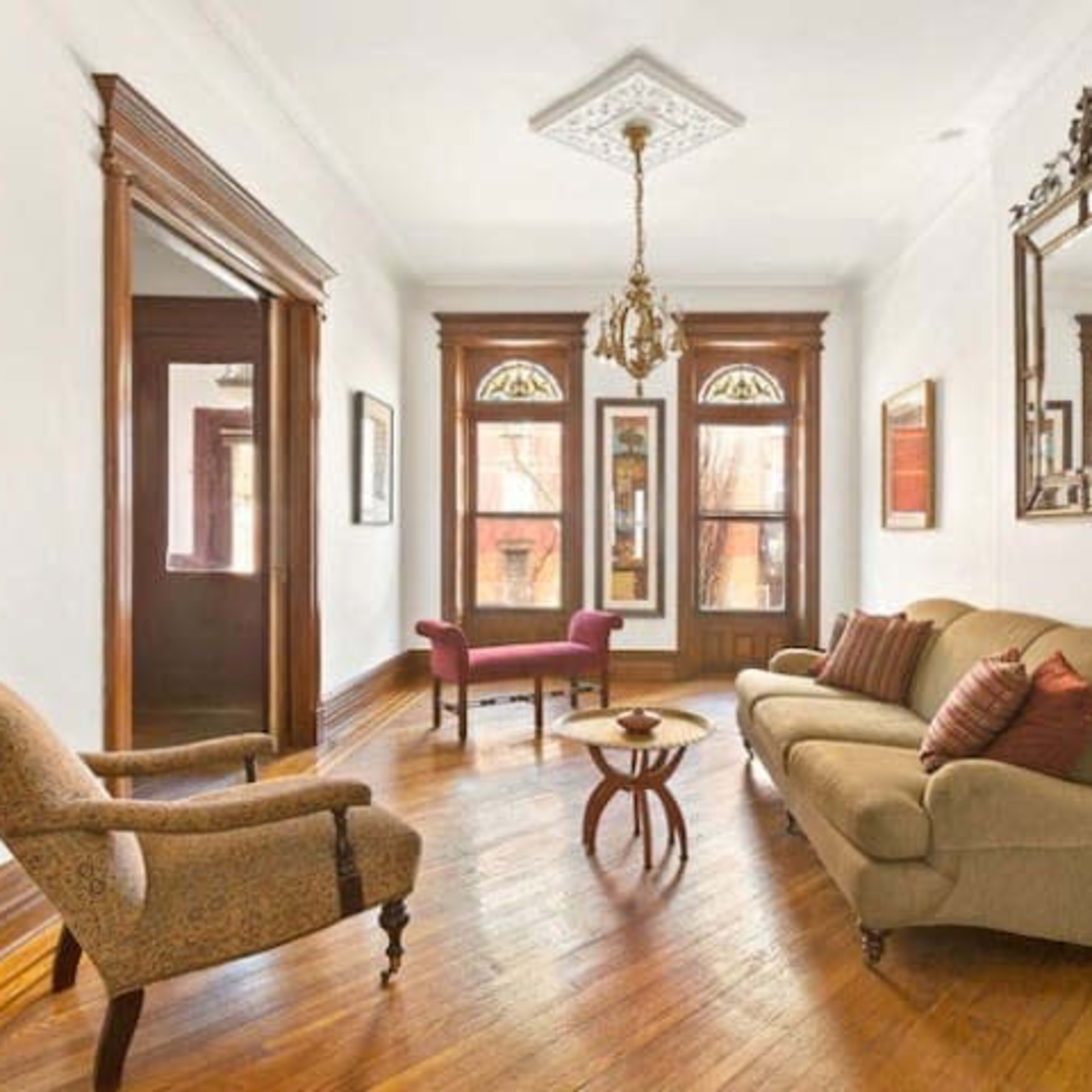 A living room with hardwood floors, a brown sofa, two chairs, and framed artwork on the walls.