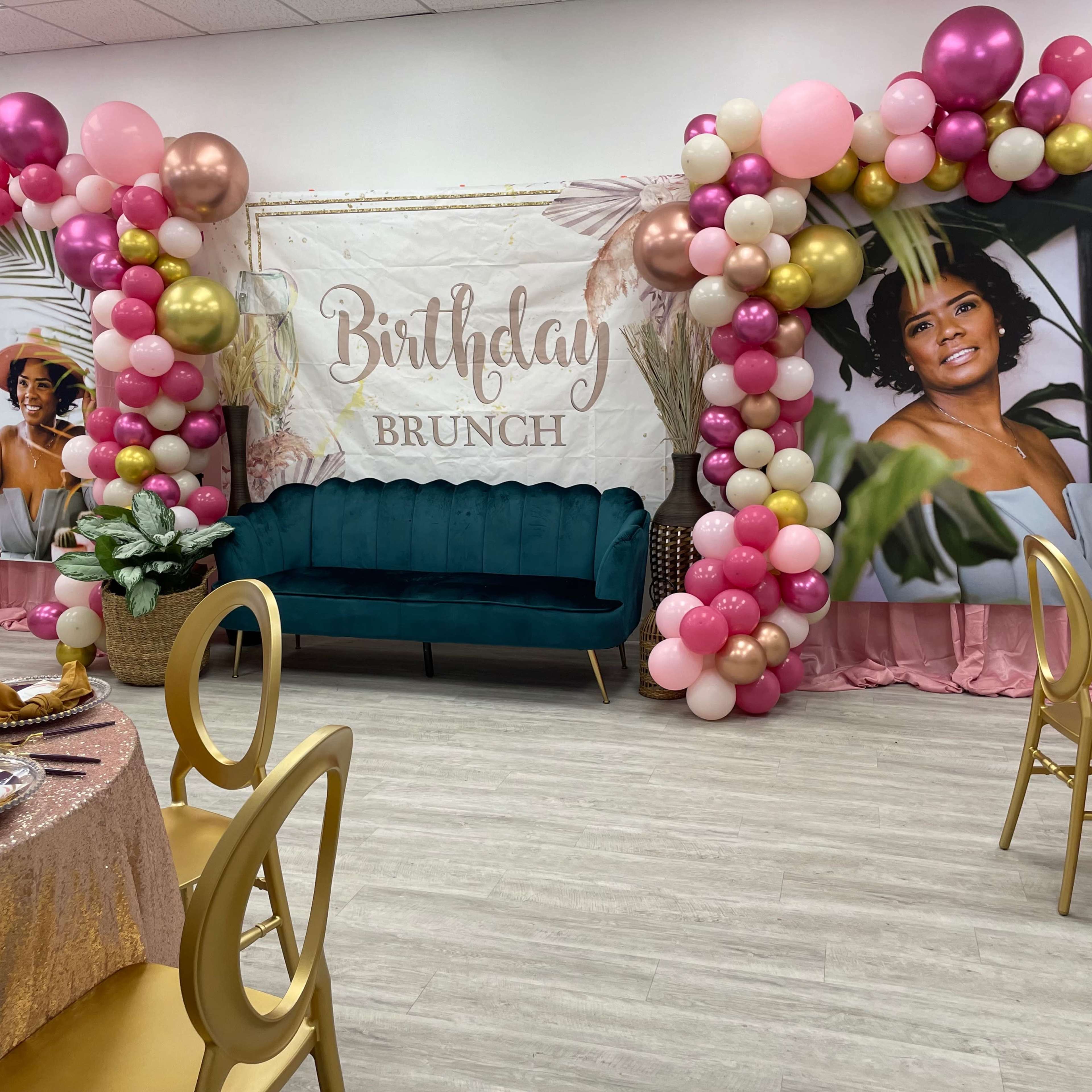 A decorated event space for a birthday brunch, featuring a balloon arch, a central sign that reads "Birthday Brunch," and tables set with golden tableware.