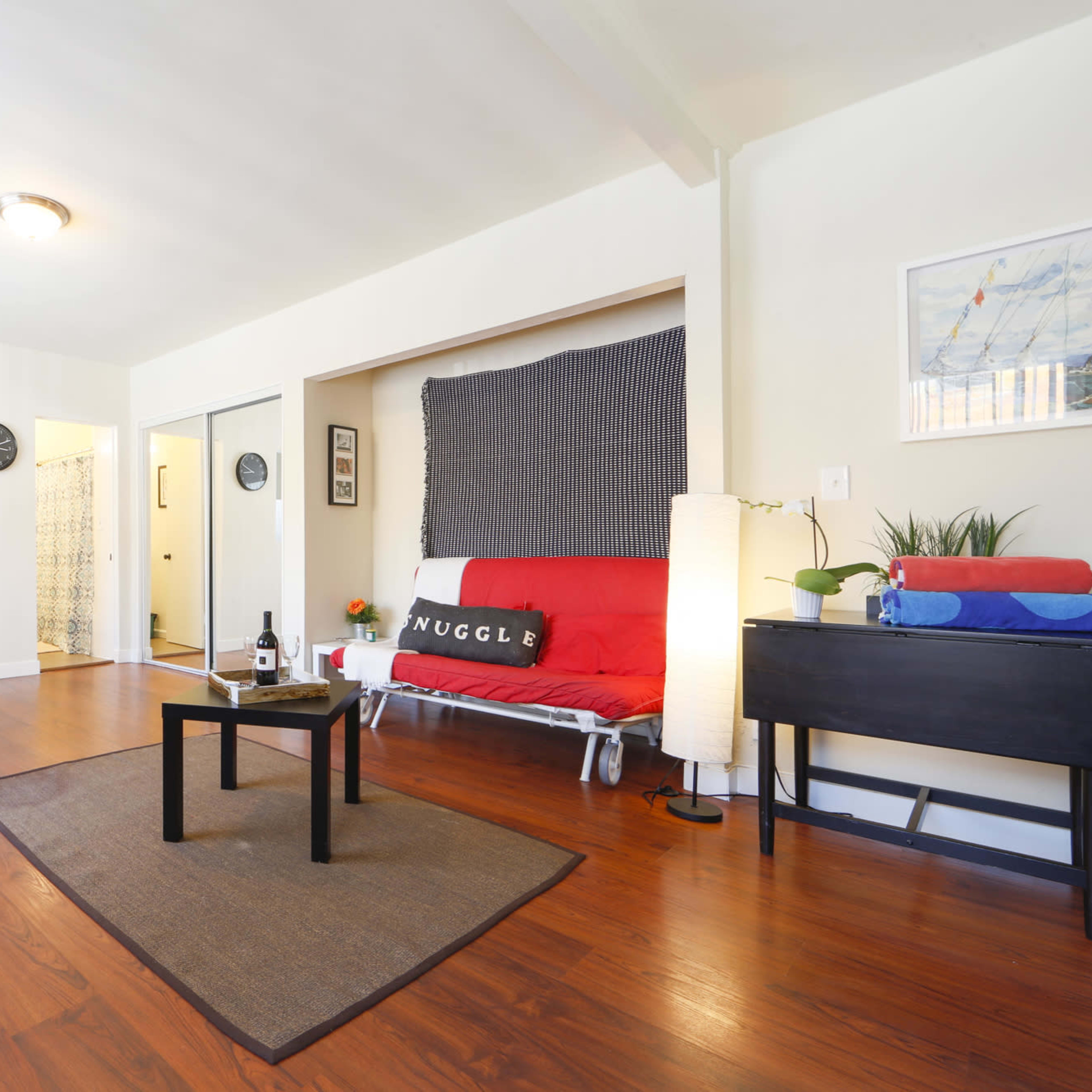 A well-lit living space with a dining area, a futon sofa, and a small table situated on a hardwood floor.