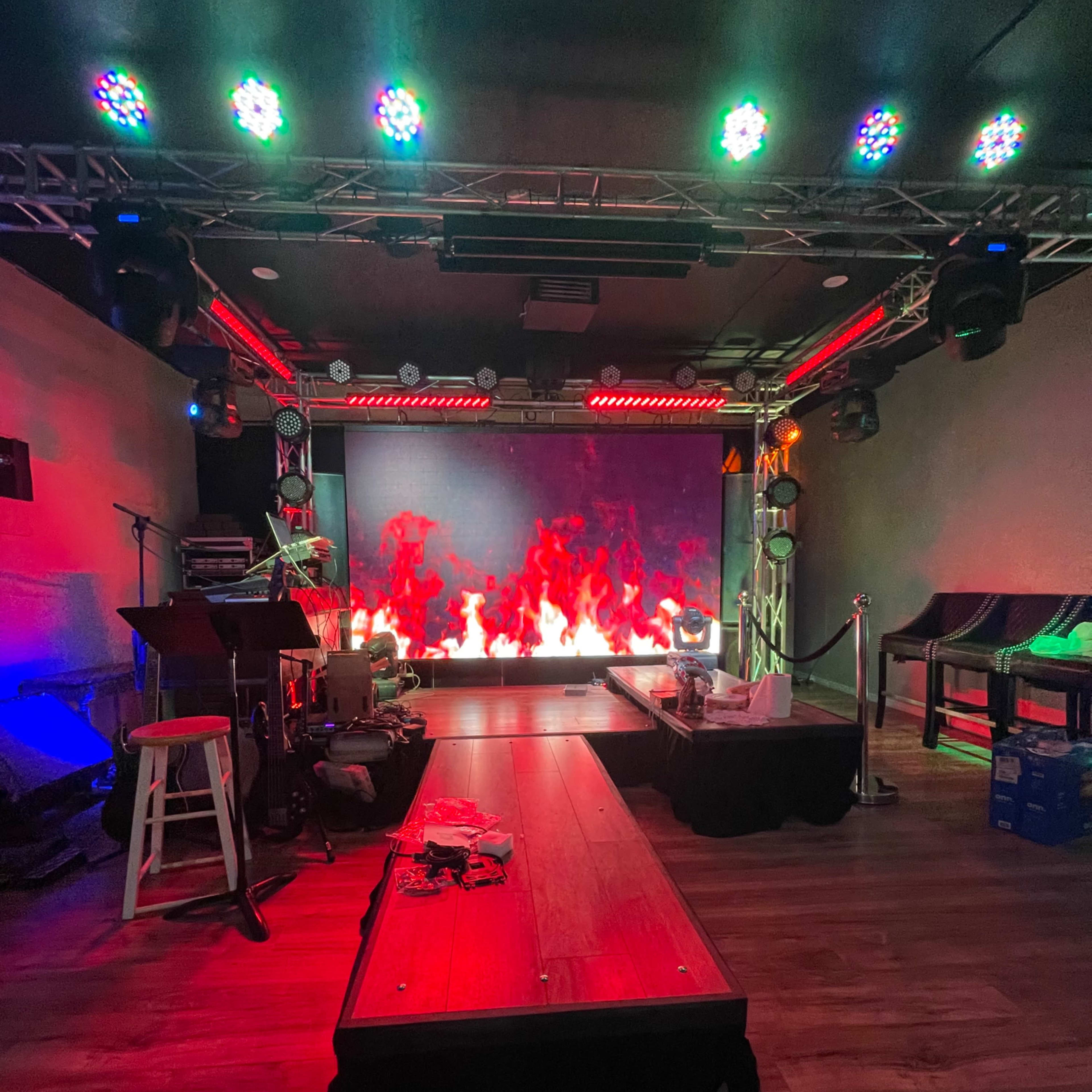 A staging area with a backdrop of digital flames, illuminated by colorful stage lights, and a wooden platform in the foreground.