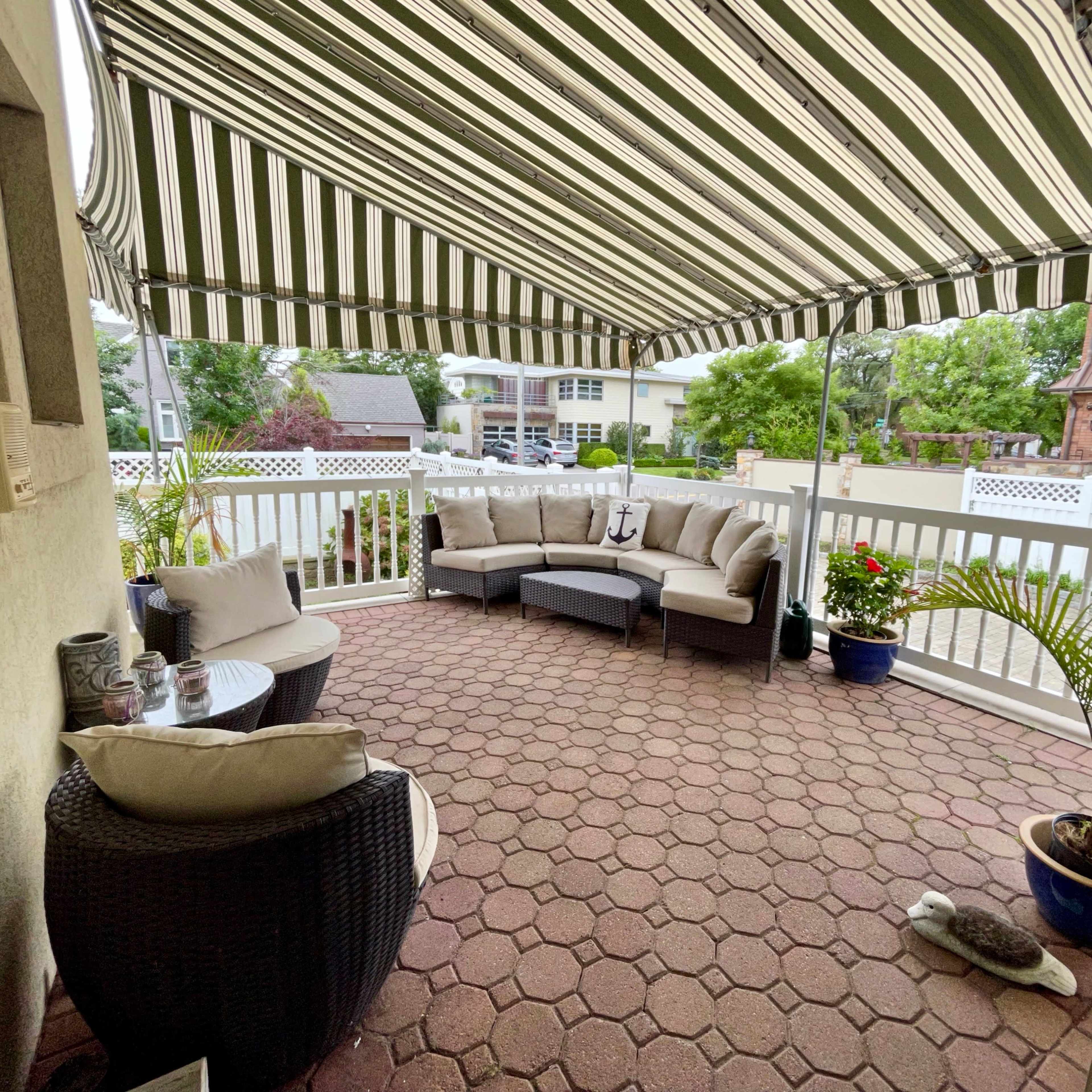 A covered patio features a seating arrangement with a sectional sofa, armchairs, and decorative plants.