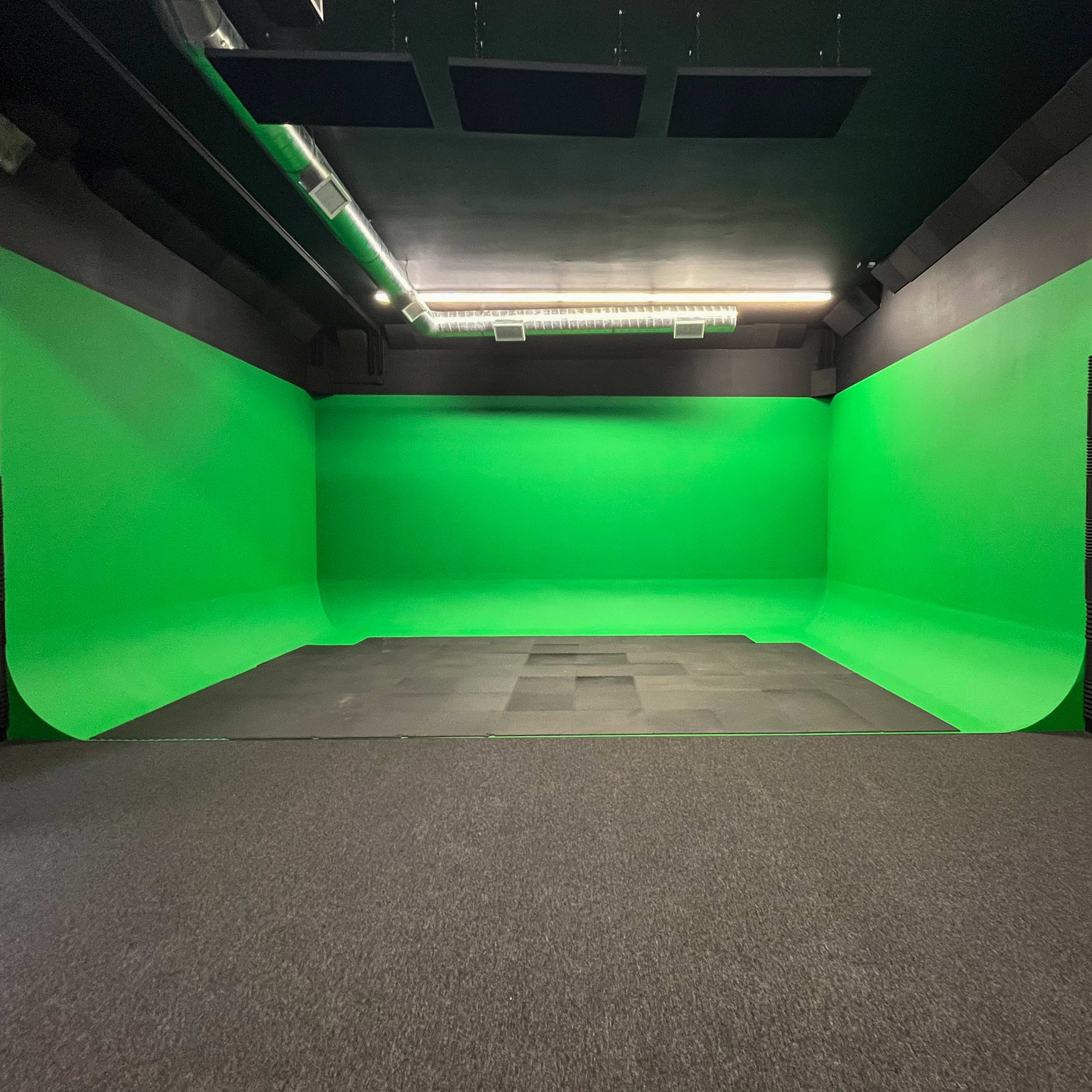 A studio space featuring green screen walls and a seamless green floor.