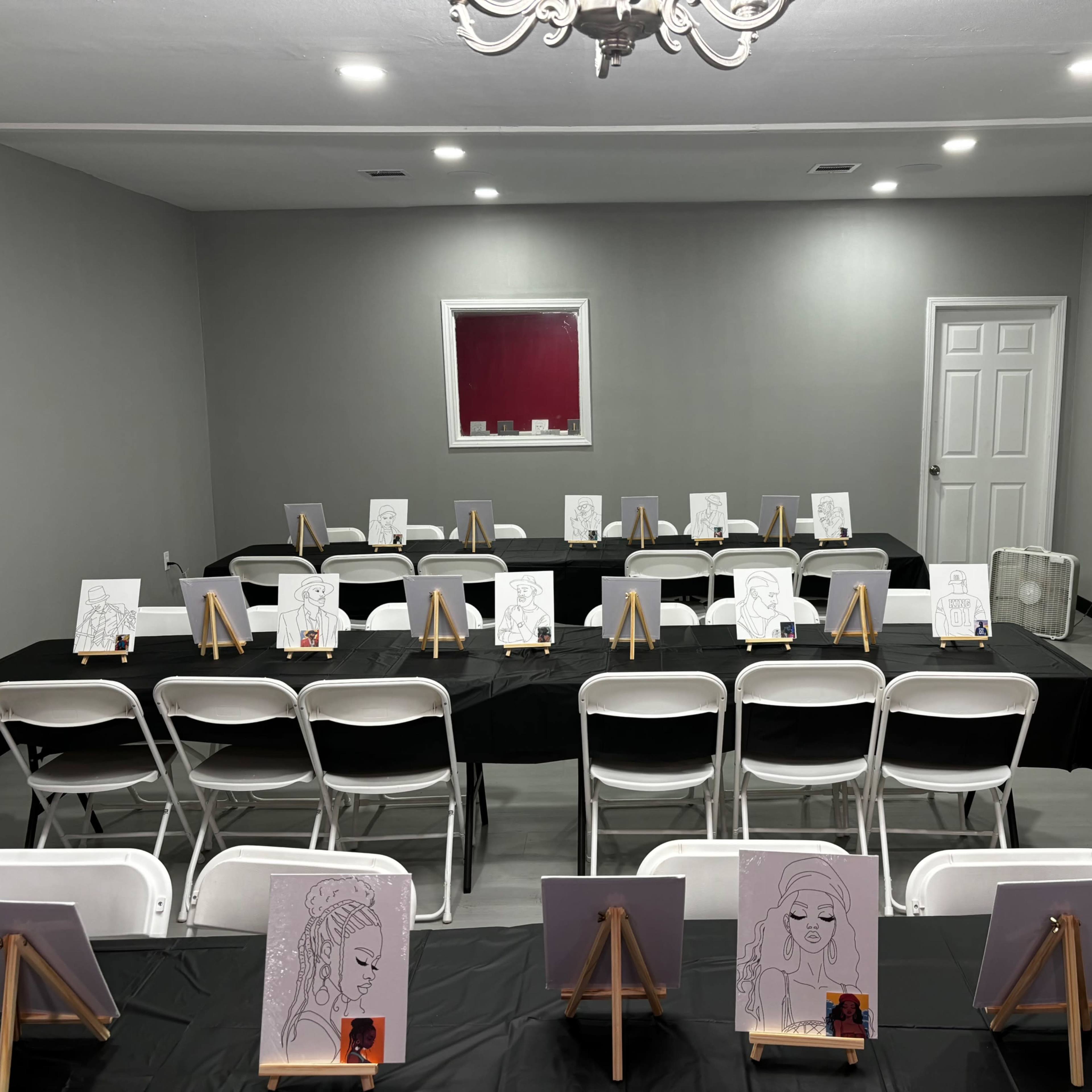 The room features rows of white chairs facing easels with black and white sketches on each, arranged on tables covered with black cloth.