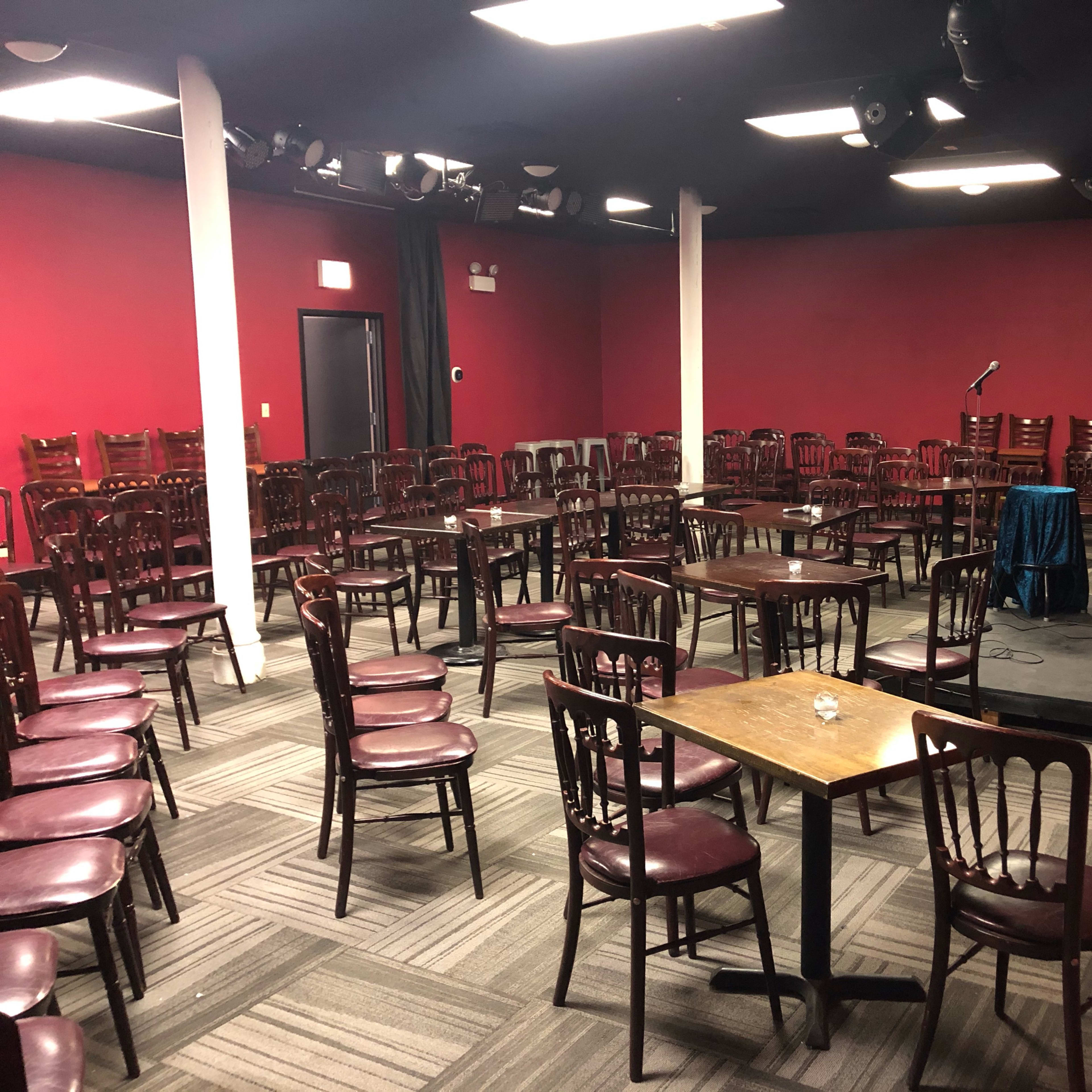 An empty performance space with arranged chairs facing a small stage equipped with a microphone and a table draped in blue.