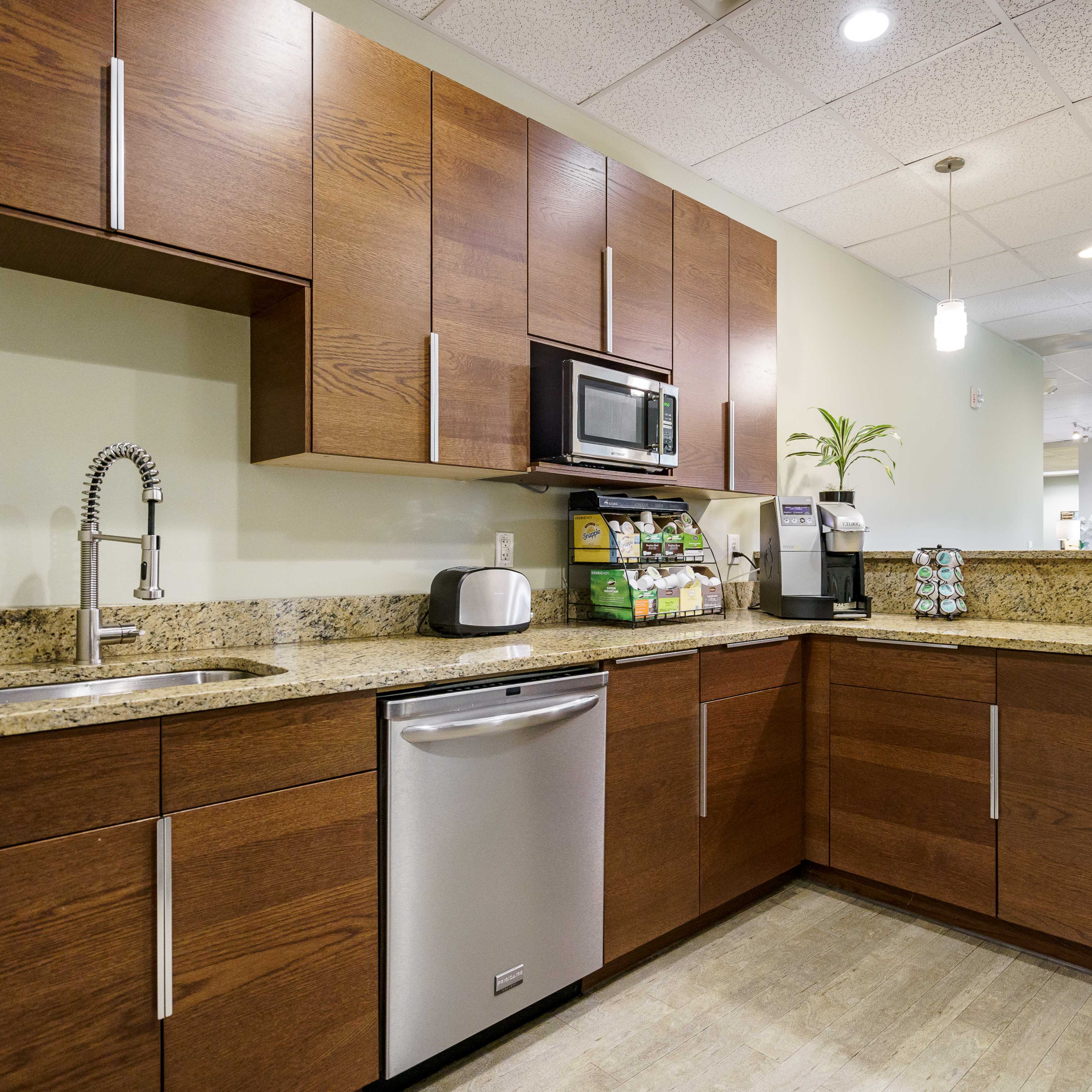 A modern kitchen with wooden cabinets, a stainless steel dishwasher, a microwave, and a countertop adorned with various kitchen appliances and a small plant.