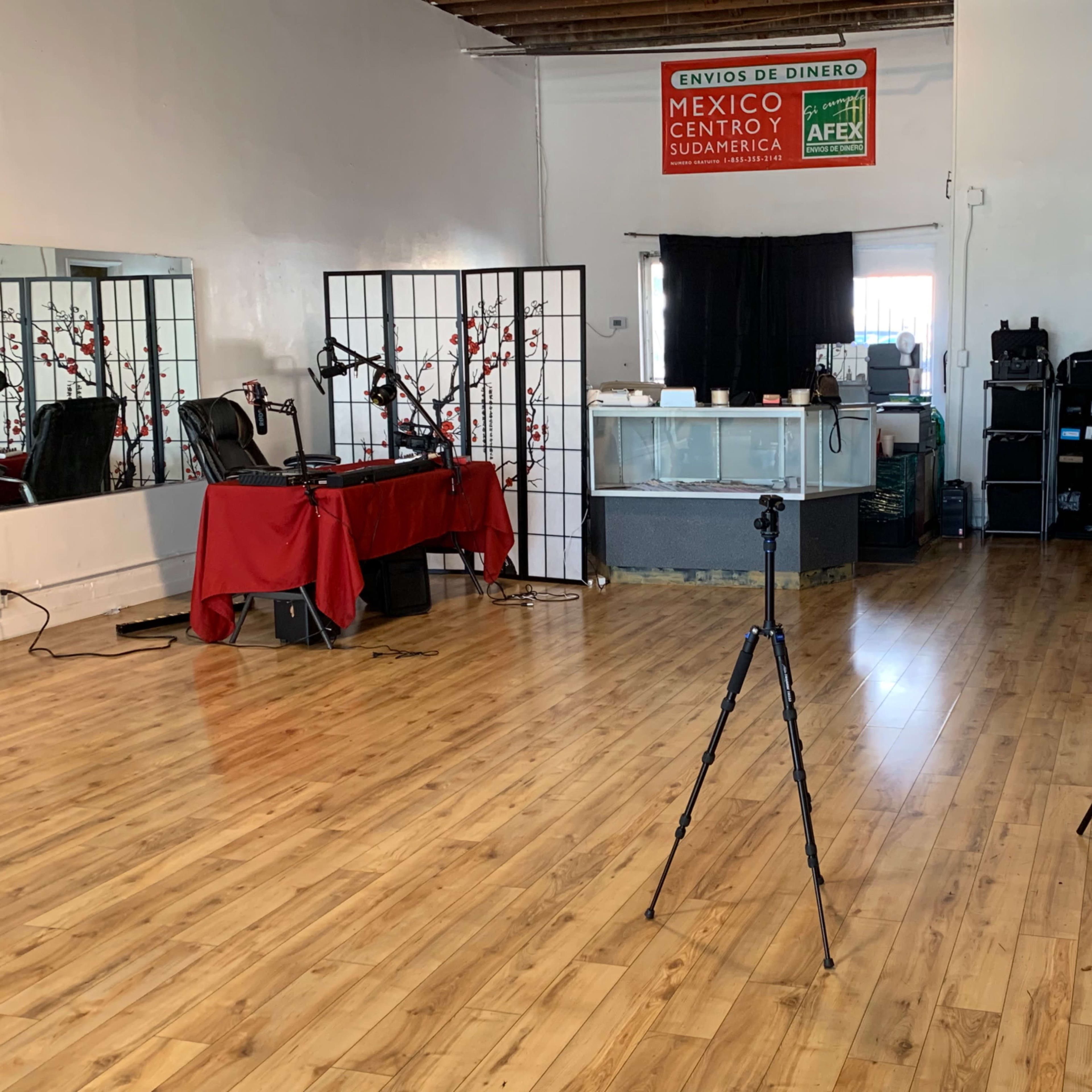 A spacious room with wooden flooring, featuring a reception area, a red tablecloth, and various equipment set up for photography or video recording.