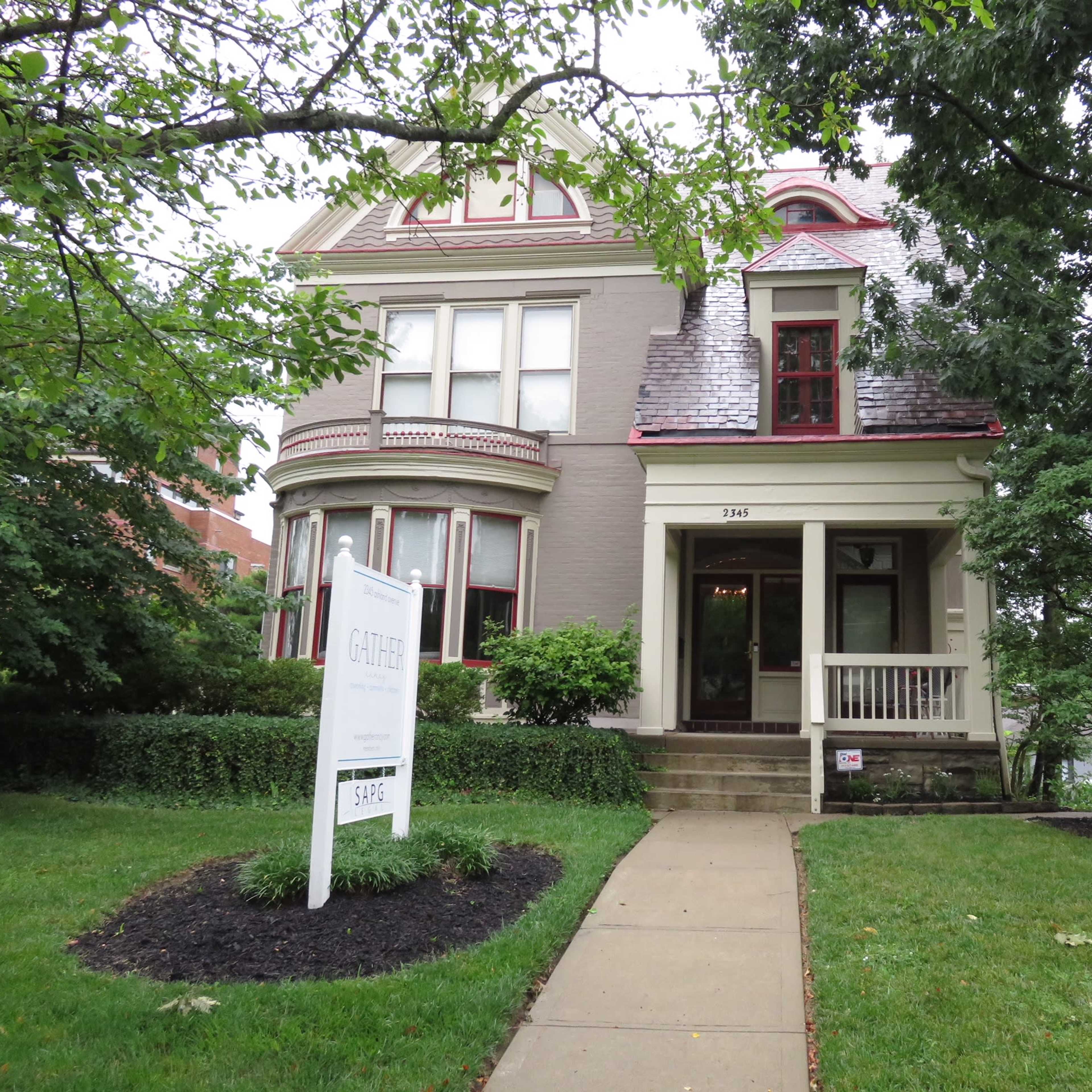 A large Victorian-style house with a gabled roof and a sign in front indicating it is for sale.