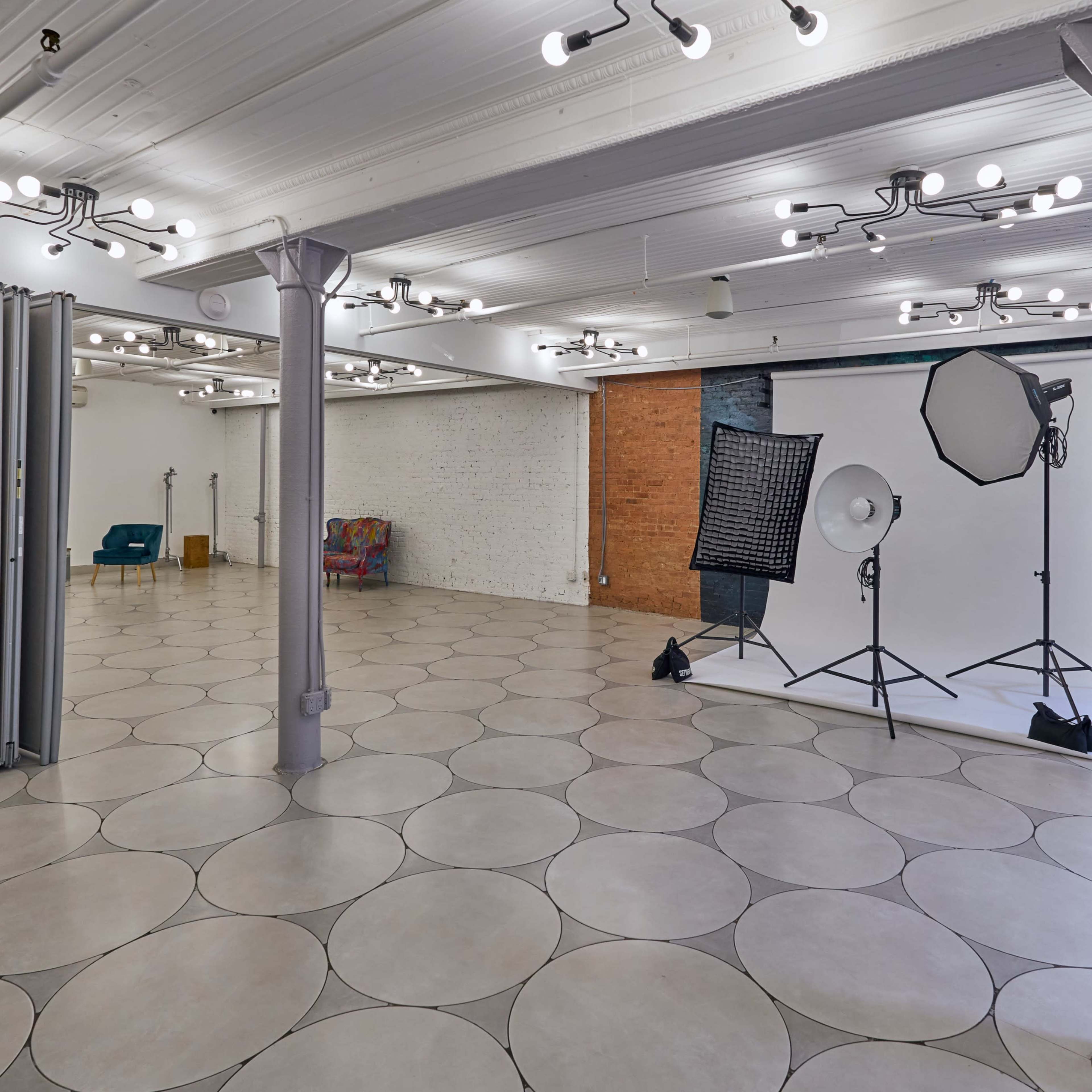 A spacious photography studio featuring a large white backdrop, lighting equipment, and a tiled floor.