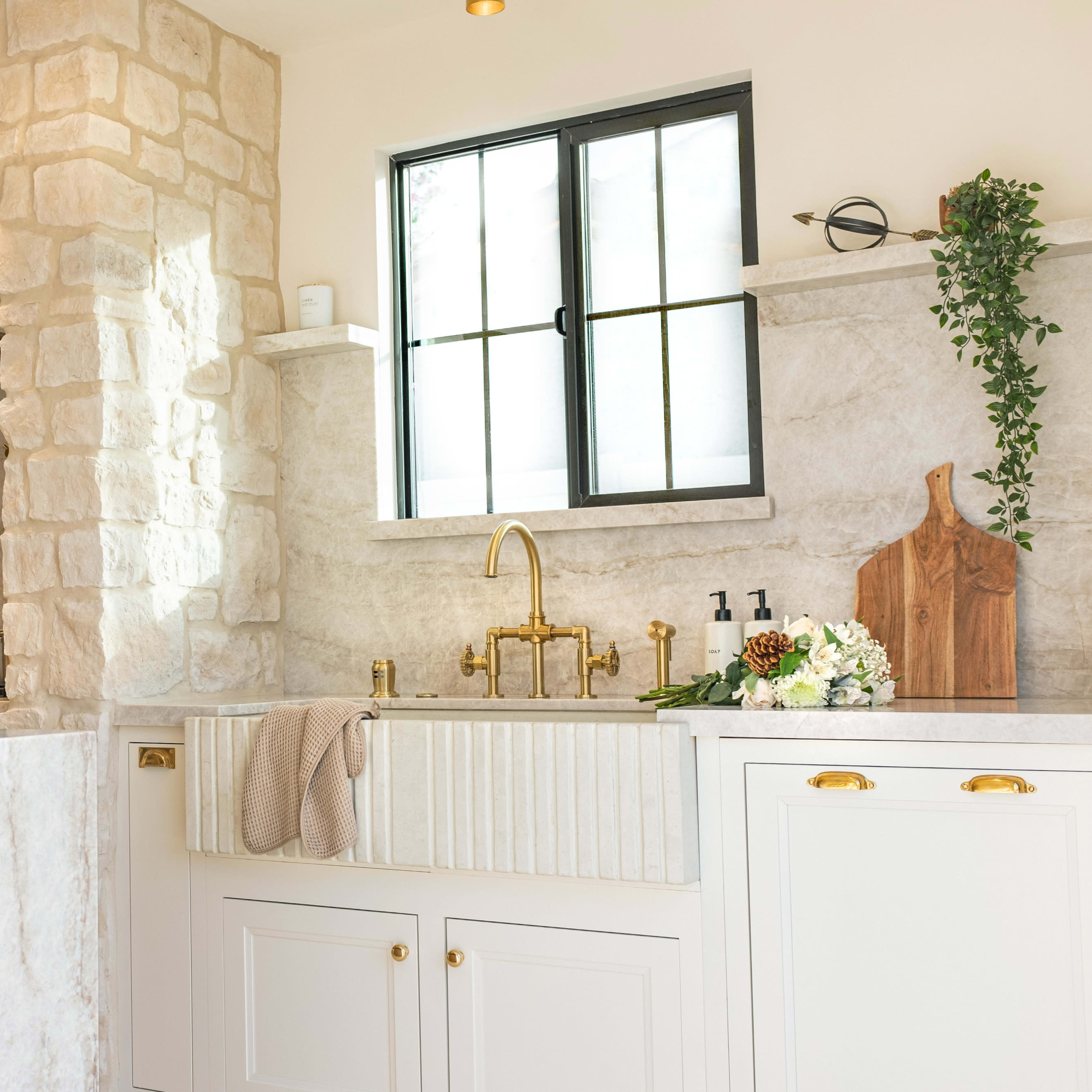A kitchen with a marble countertop, a farmhouse sink, stone walls, and modern fixtures.