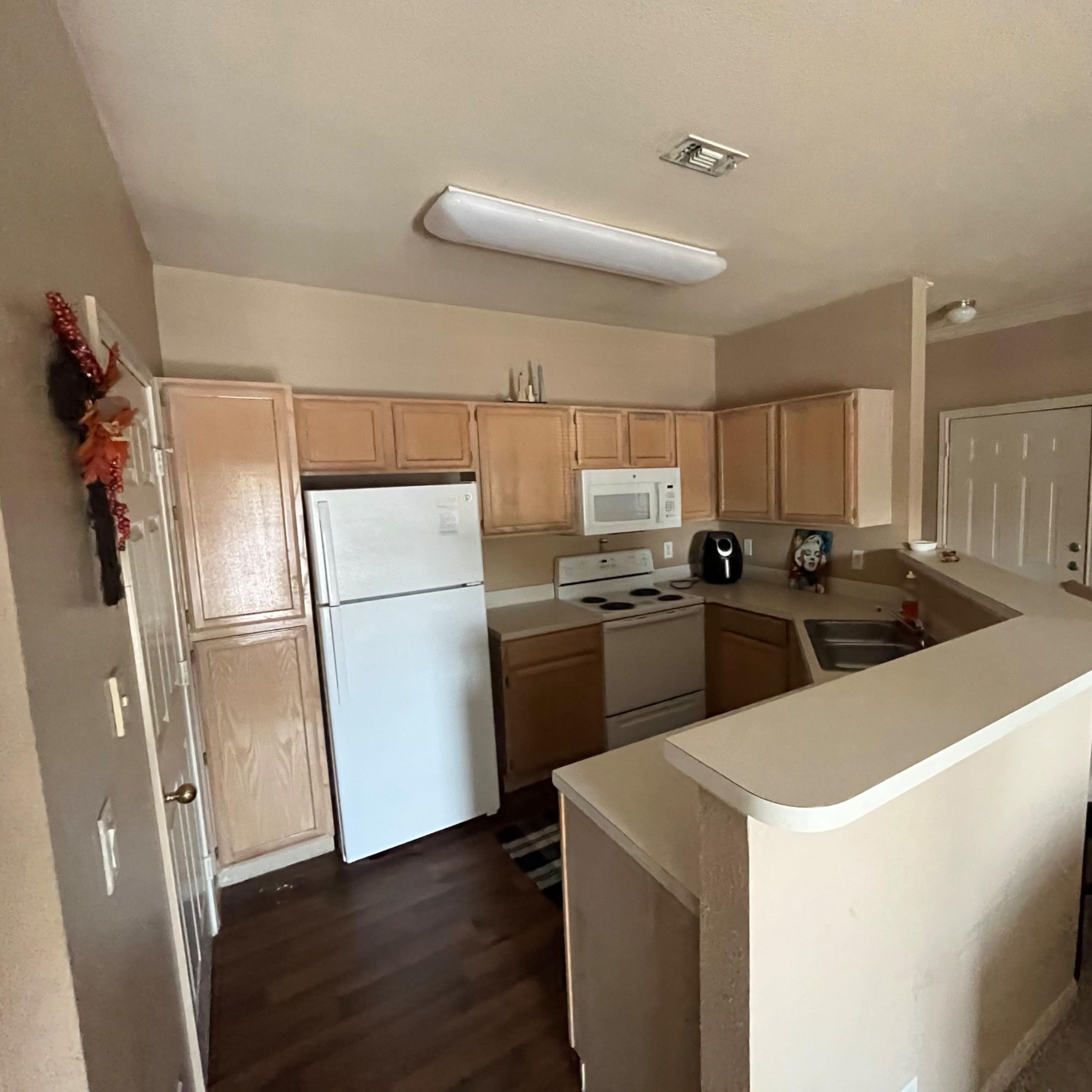 A kitchen features light wooden cabinets, white appliances, and a small breakfast bar with a chair.