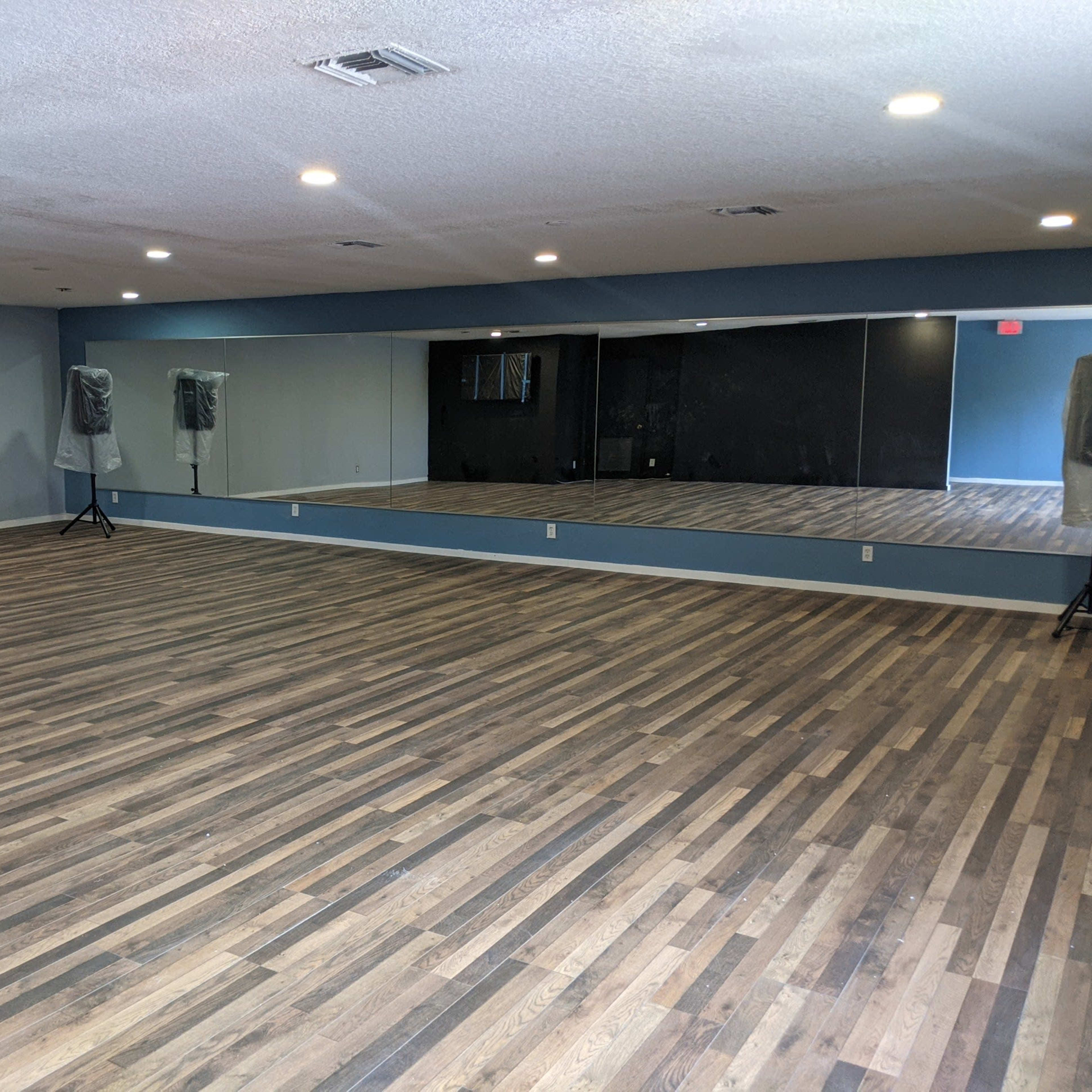 An empty dance studio with wooden flooring and large mirrors on one wall.