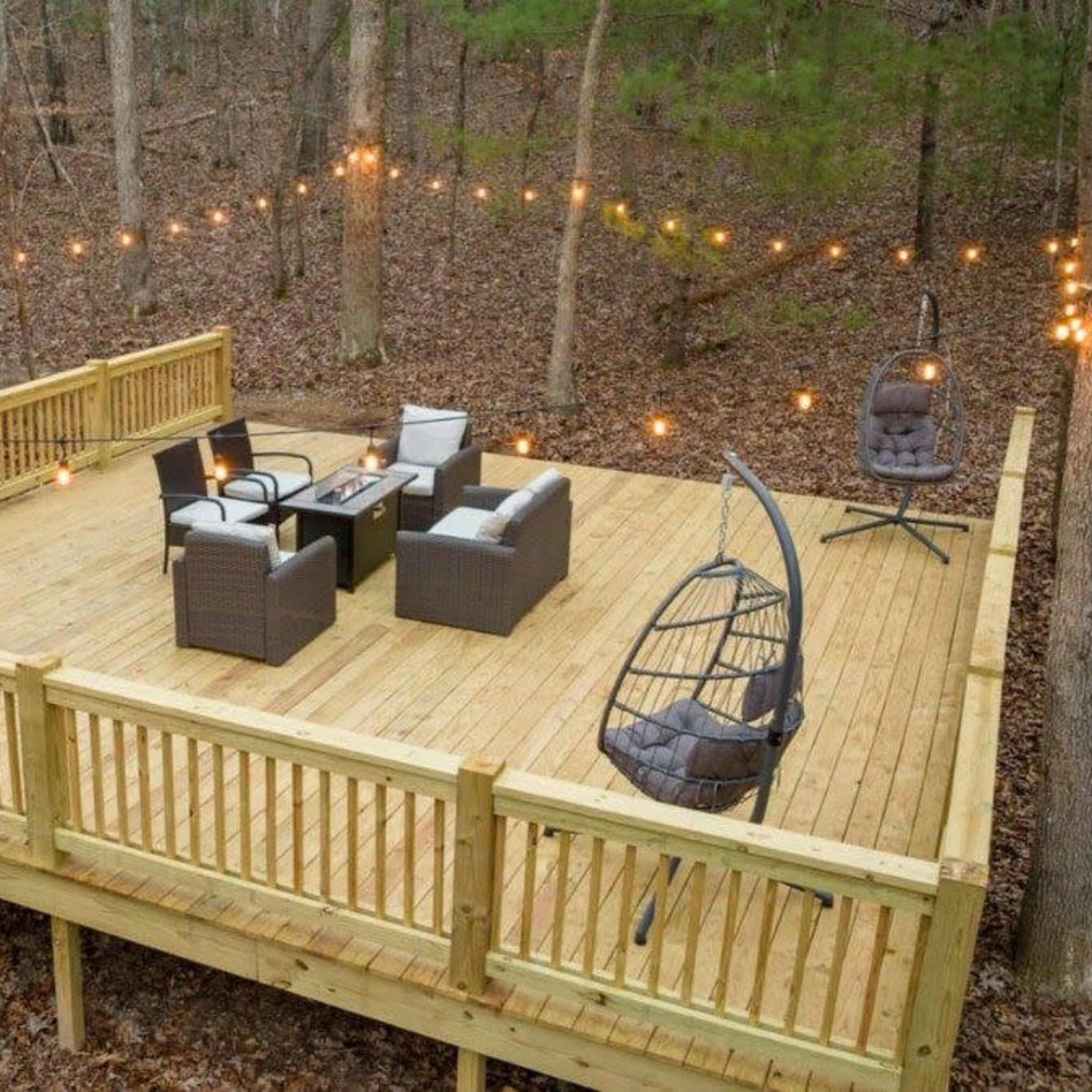 A wooden deck in a forested area features outdoor seating and string lights overhead.