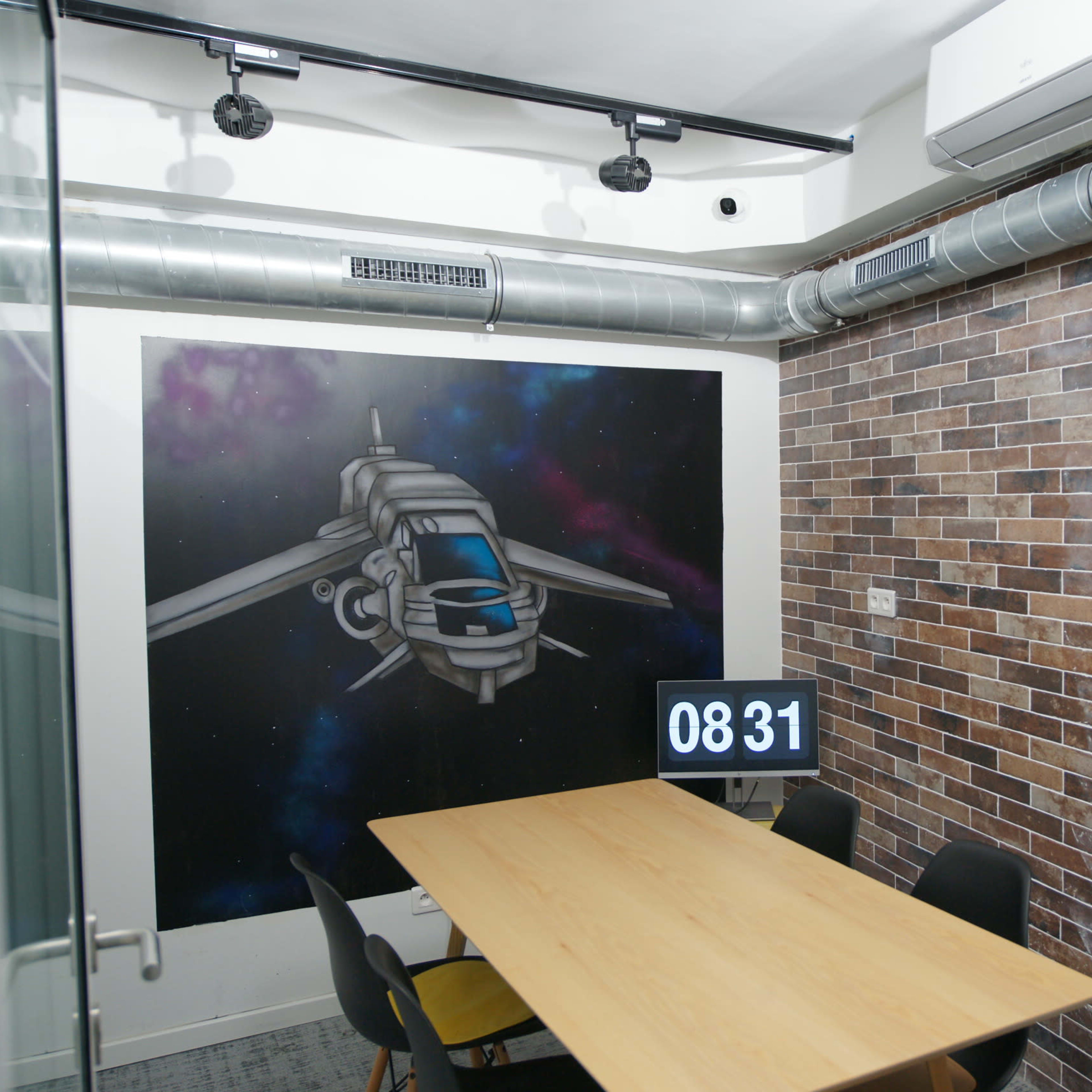 A modern meeting room with a brick wall, a large wooden table, and a mural of a spaceship.