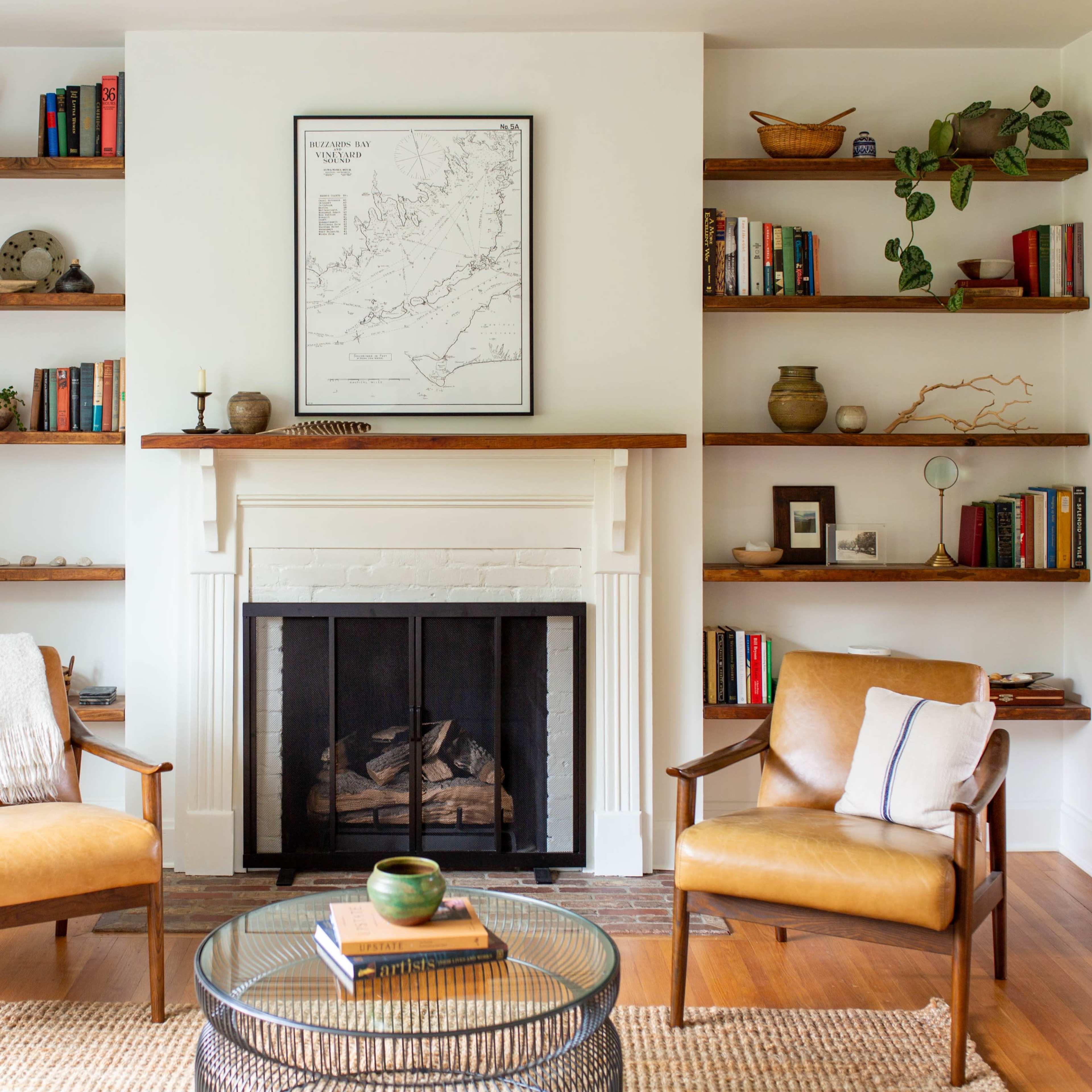 A cozy living room features two leather chairs facing a fireplace, with bookshelves filled with books and decorative items on either side.