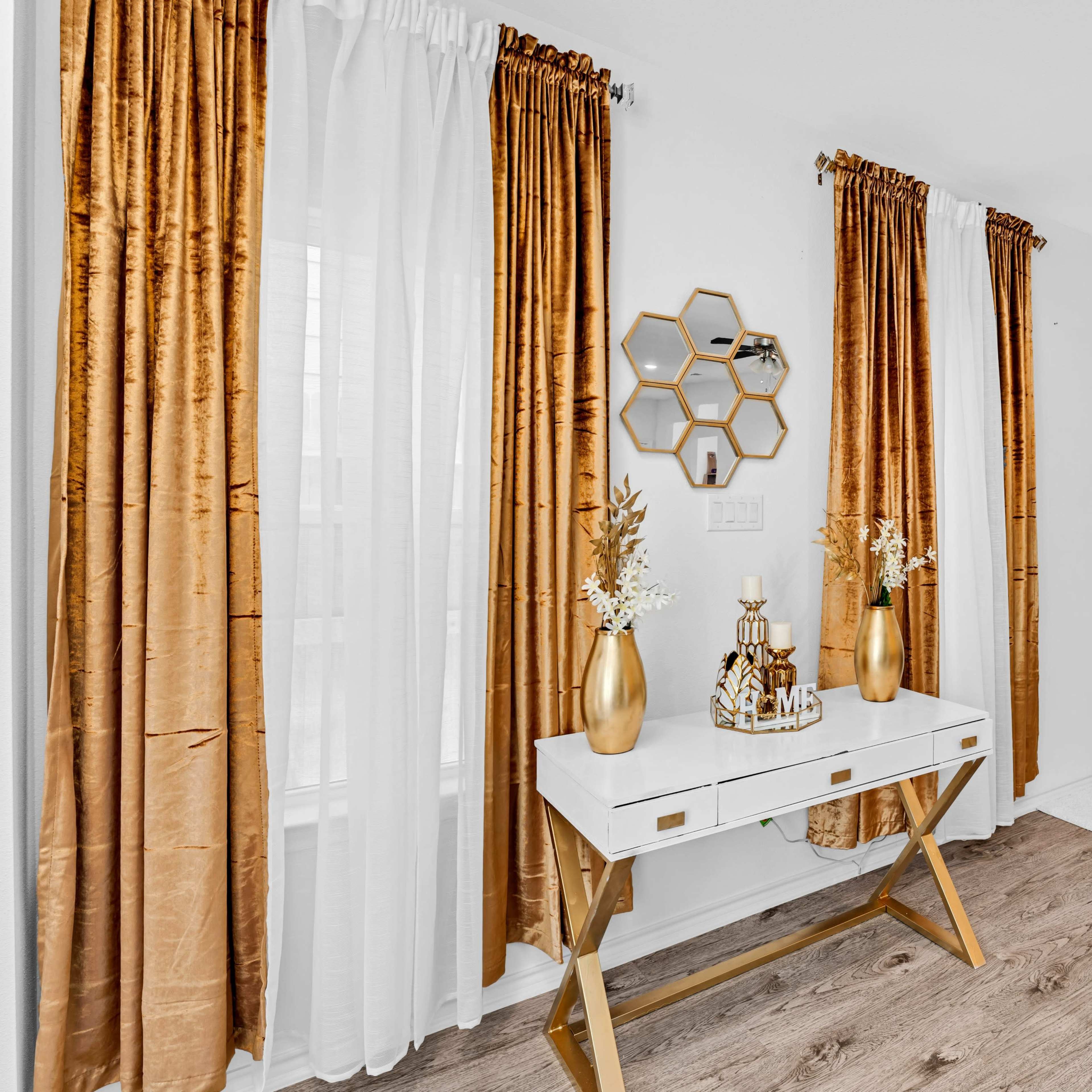 A dining area with a white table and beige chairs, surrounded by gold-accented decor and curtains, alongside a decorative mirror.