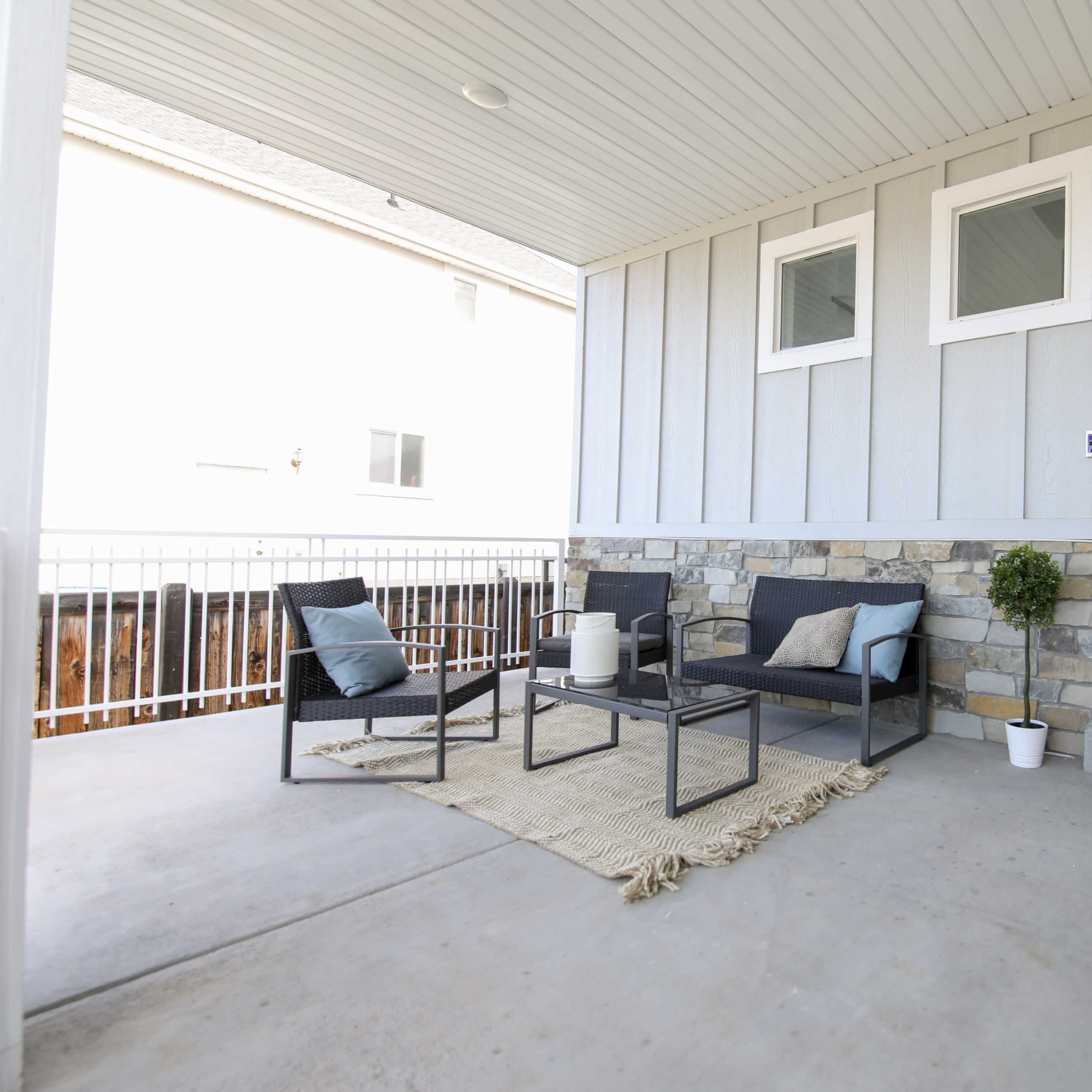 A covered porch featuring a seating area with two chairs, a small table, a welcome mat, and a decorative plant by the door.