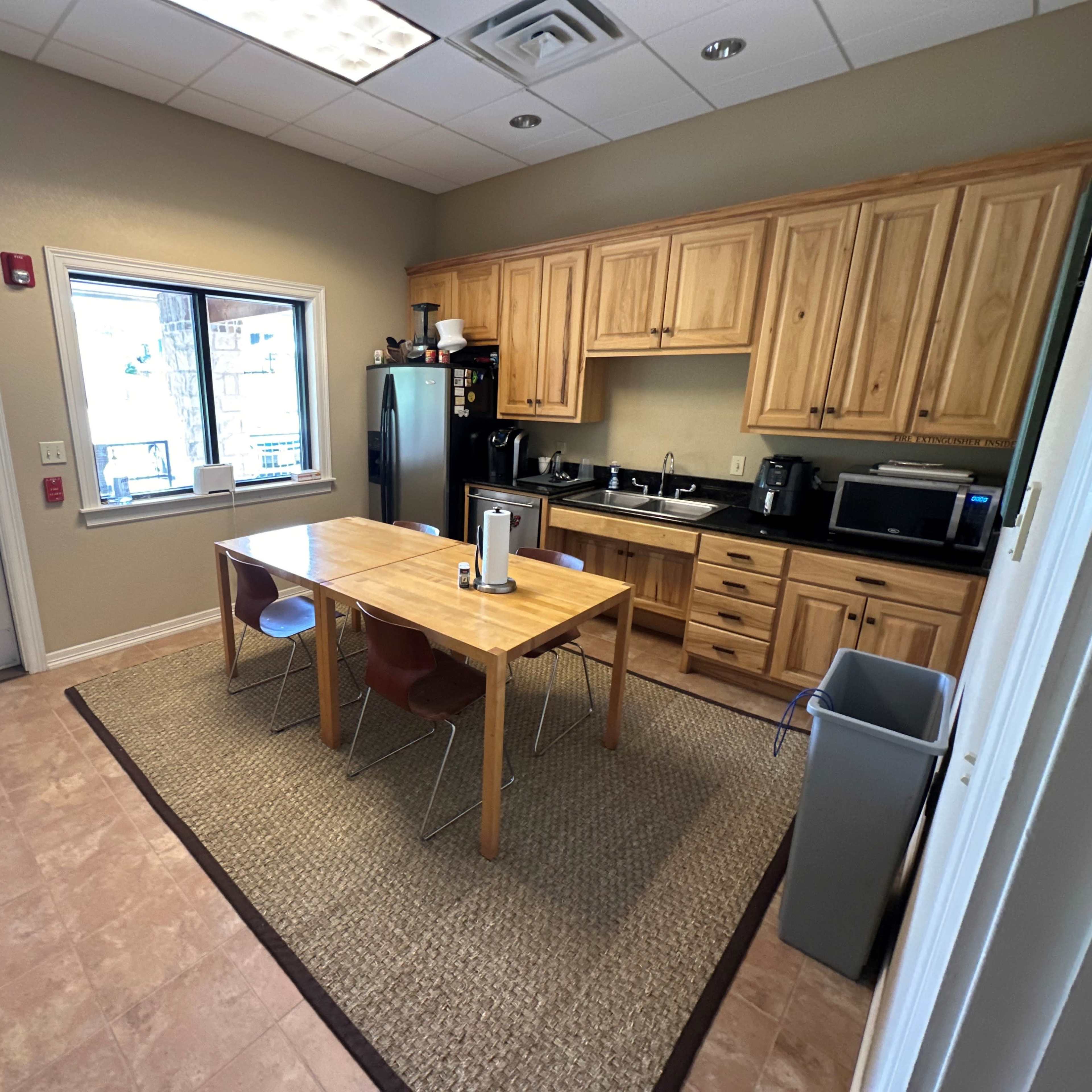 A kitchen area features wooden cabinets, a table with four chairs, and appliances along the counters, with a door and window providing access to the outside.