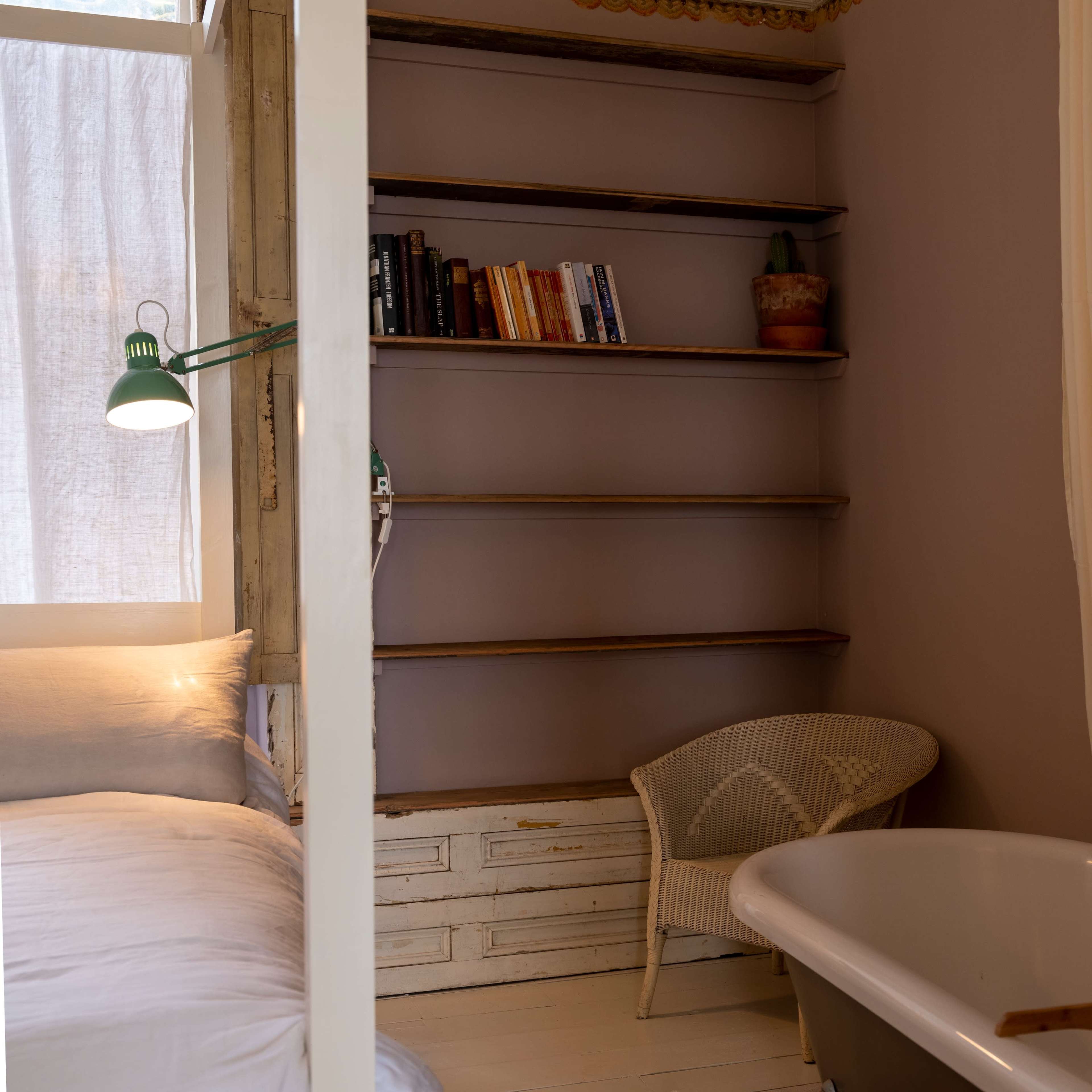 A cozy room with a bed, a bookshelf against the wall, and a freestanding bathtub beside a chair.