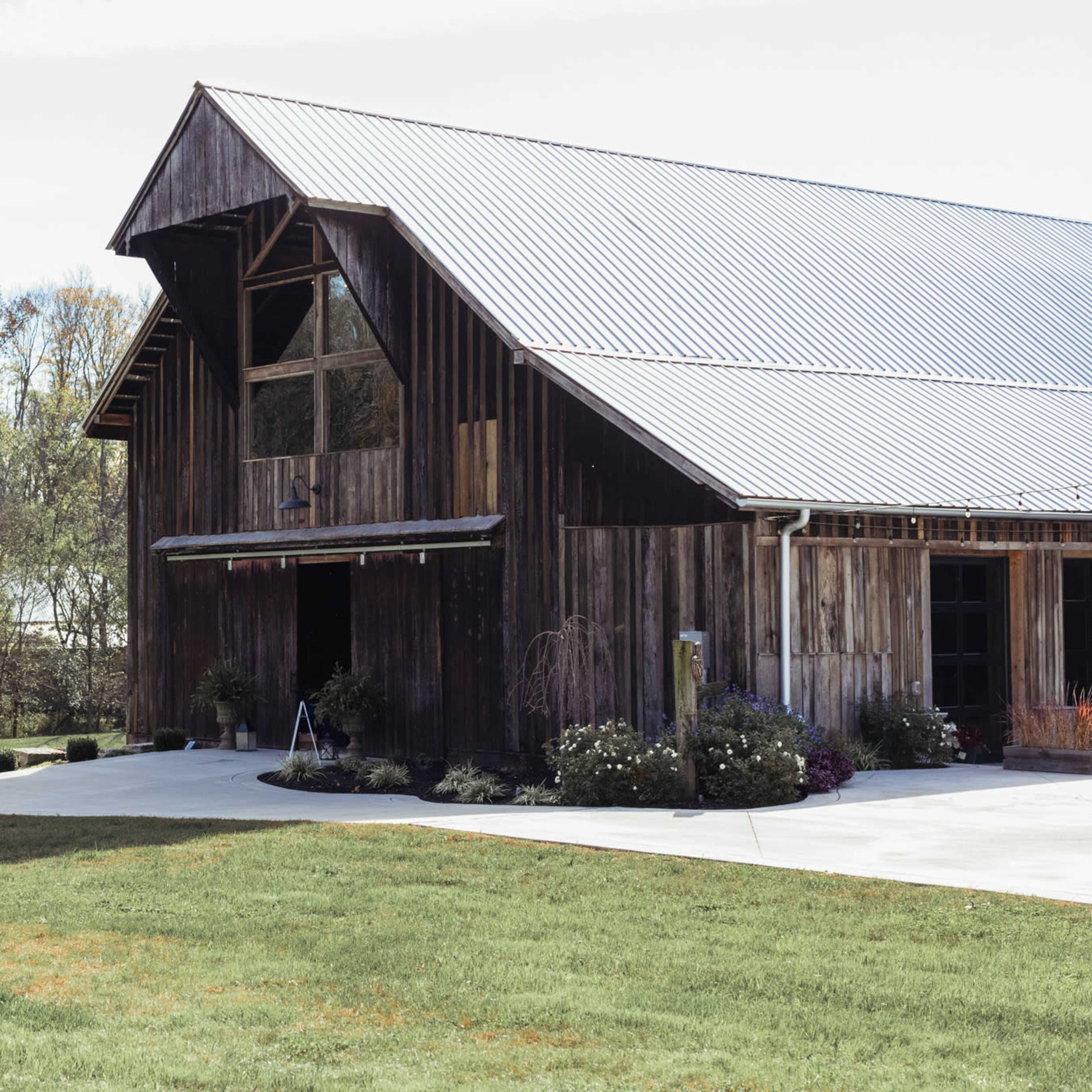 A large wooden barn with a metal roof is surrounded by green grass and trees in the background.