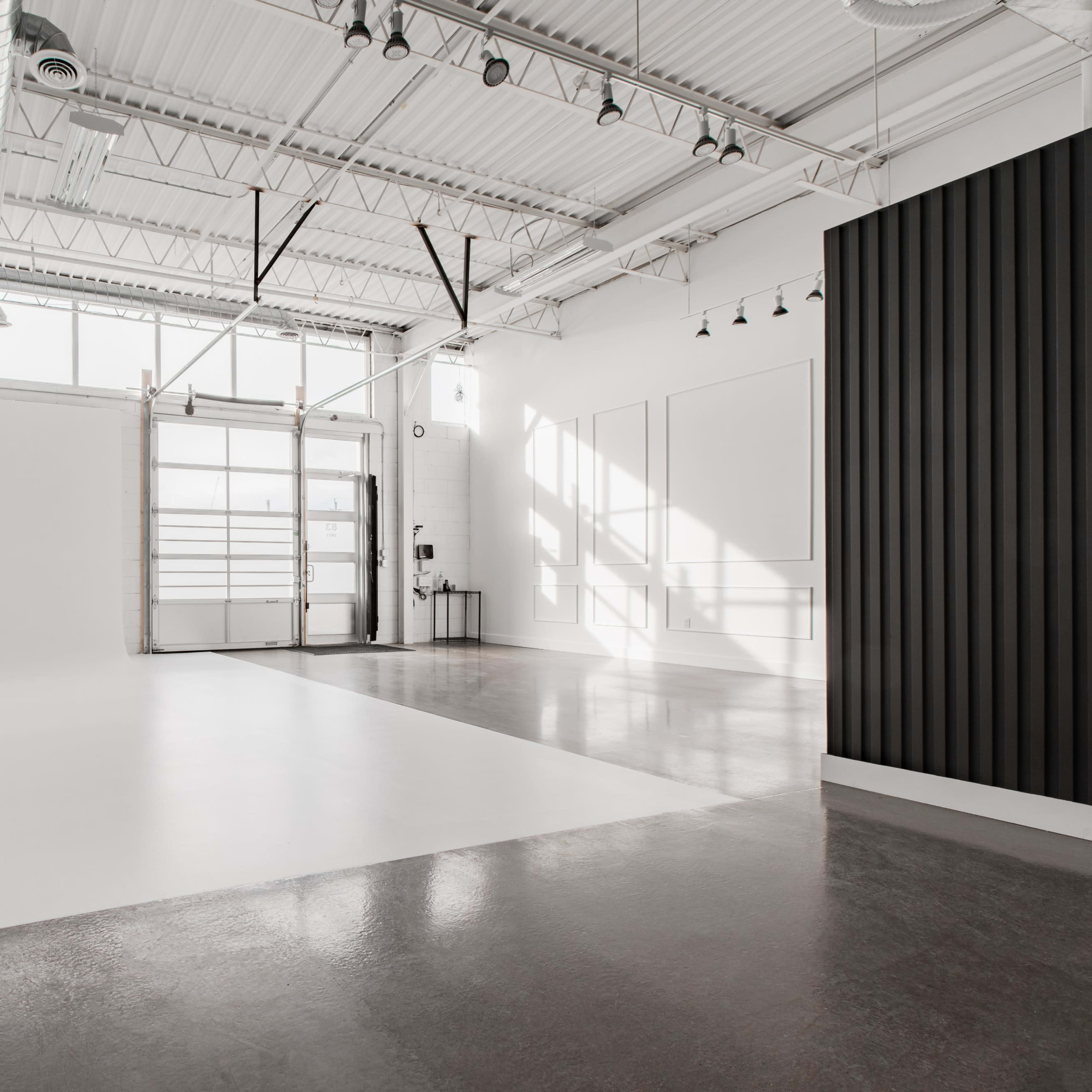 A spacious, well-lit studio with a white backdrop, polished concrete floor, and large windows.