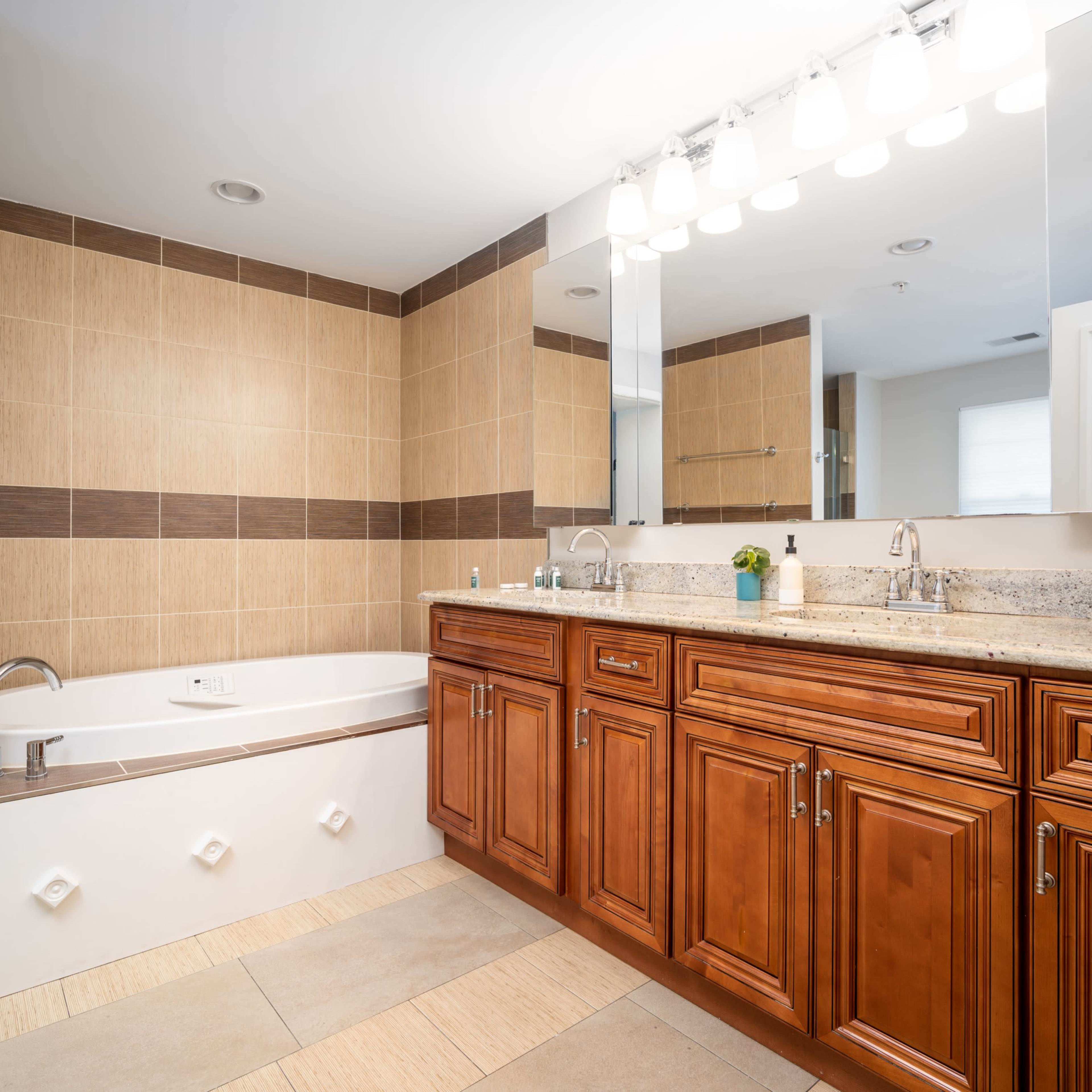 A modern bathroom features a bathtub adjacent to a double vanity with wooden cabinets and a large mirror above it.