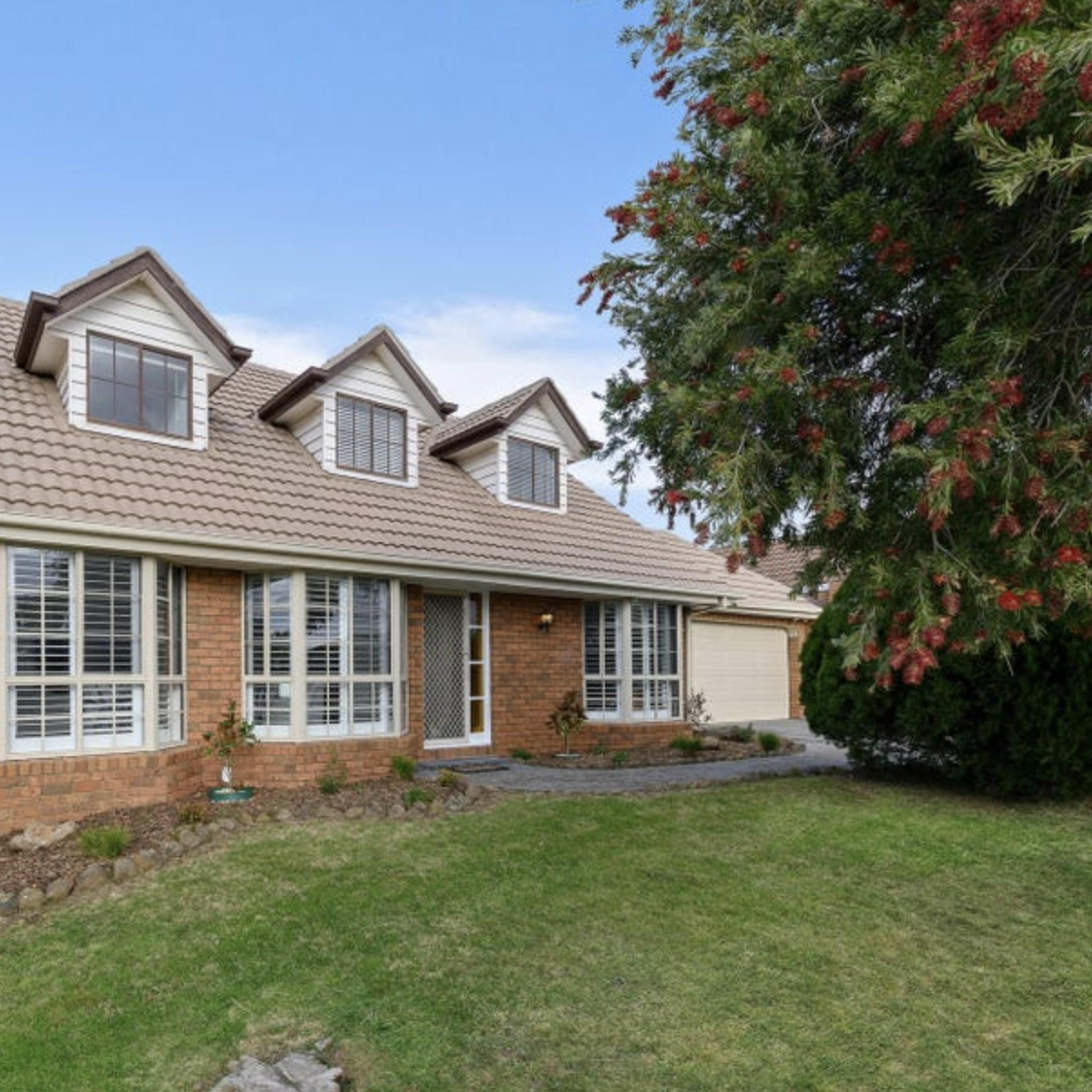 A two-story brick house with a gabled roof, surrounded by landscaped grass and shrubbery.
