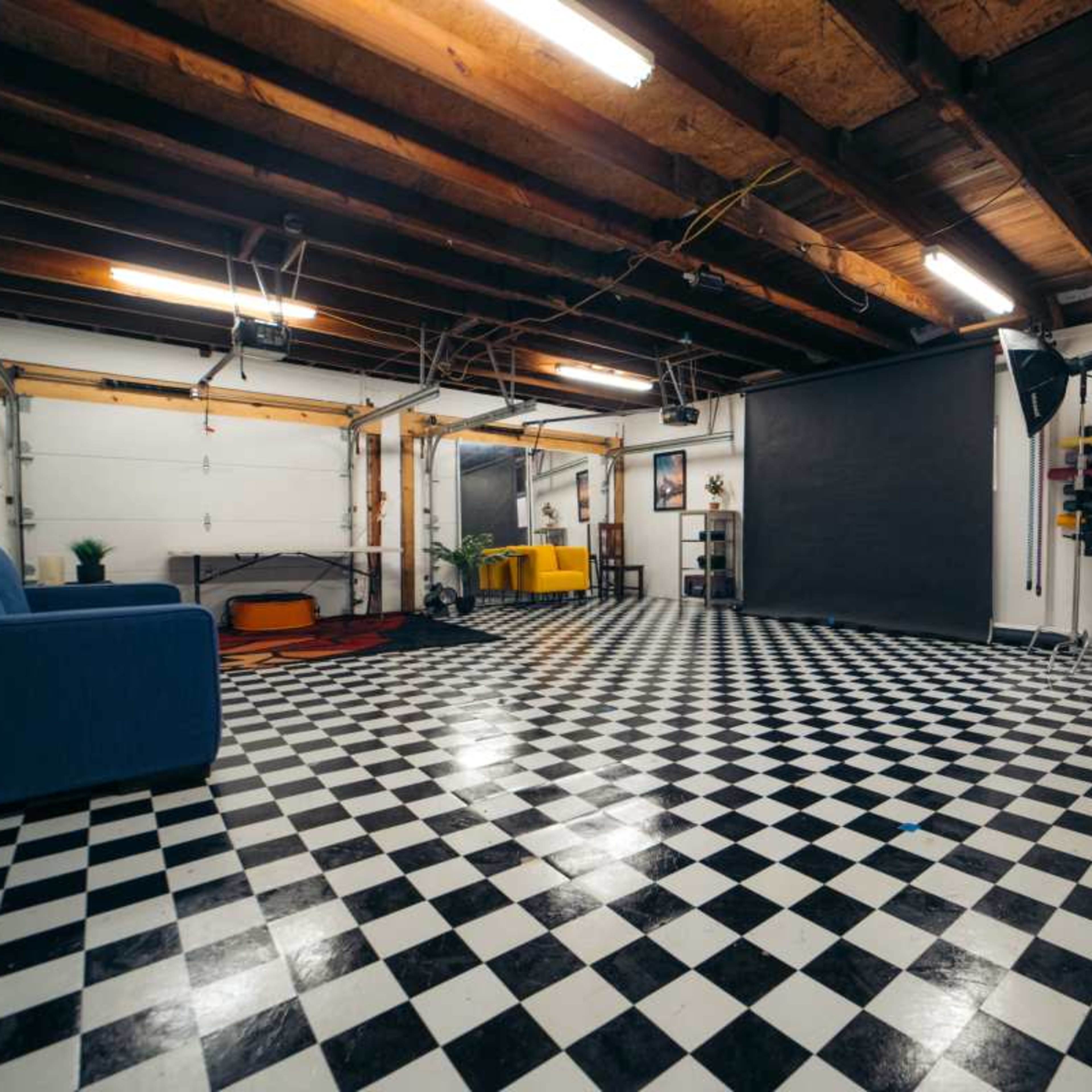 A spacious room with a black and white checkered floor, a blue couch, and various furnishings against the walls.