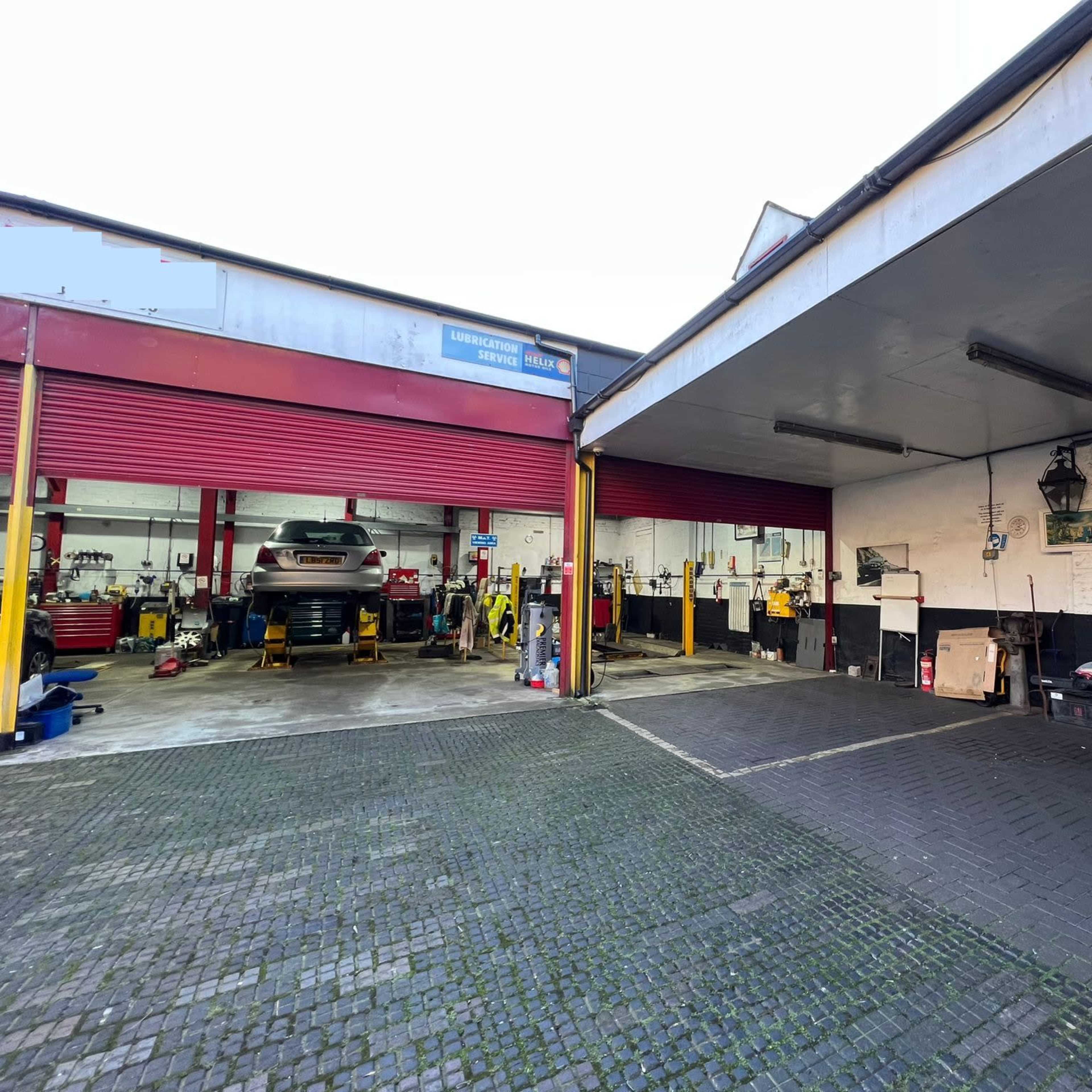 A vehicle repair shop with two service bays, one occupied by a car and various tools and equipment visible in the other bay.