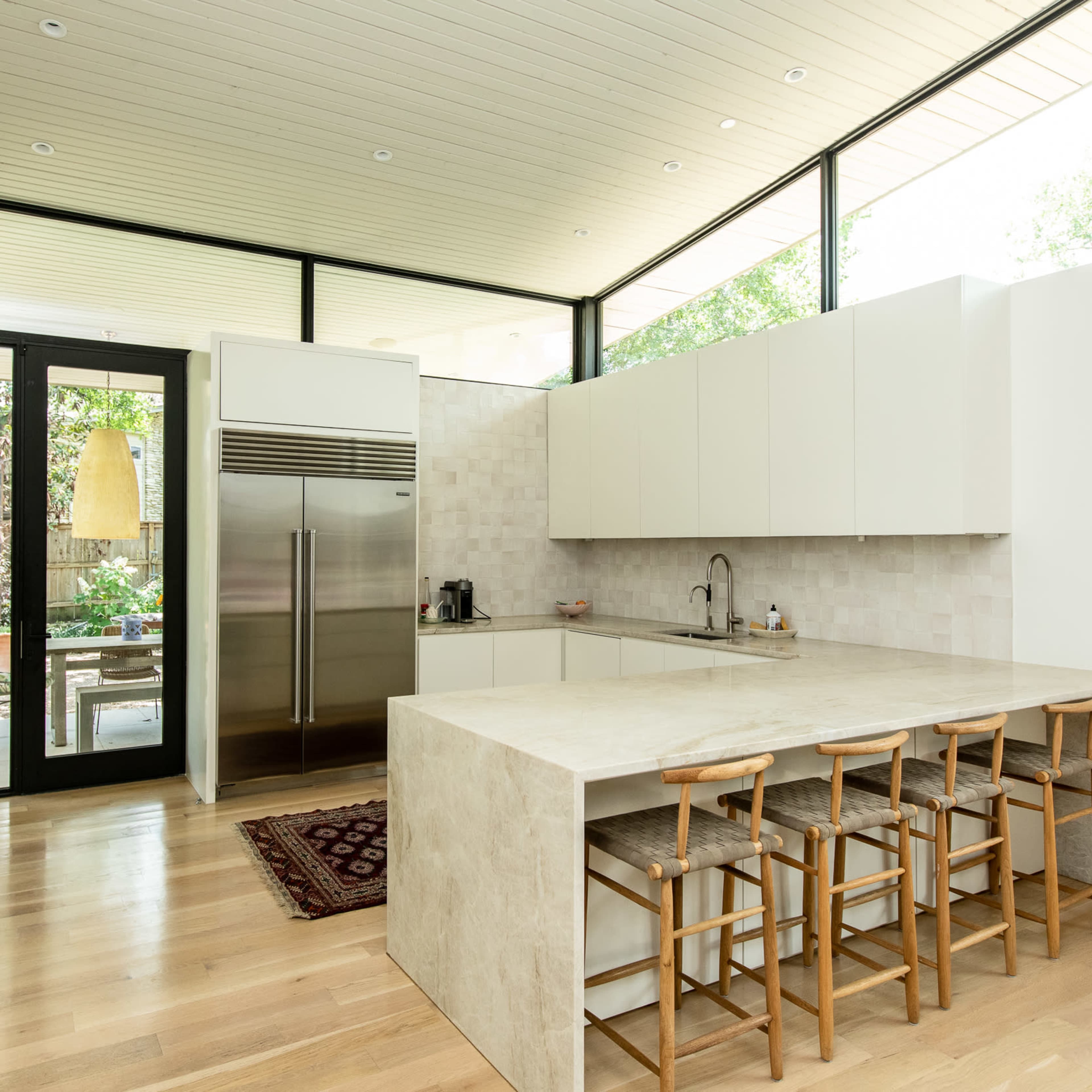 A modern kitchen with a large island, sleek cabinetry, and large windows that provide views of an outdoor garden.