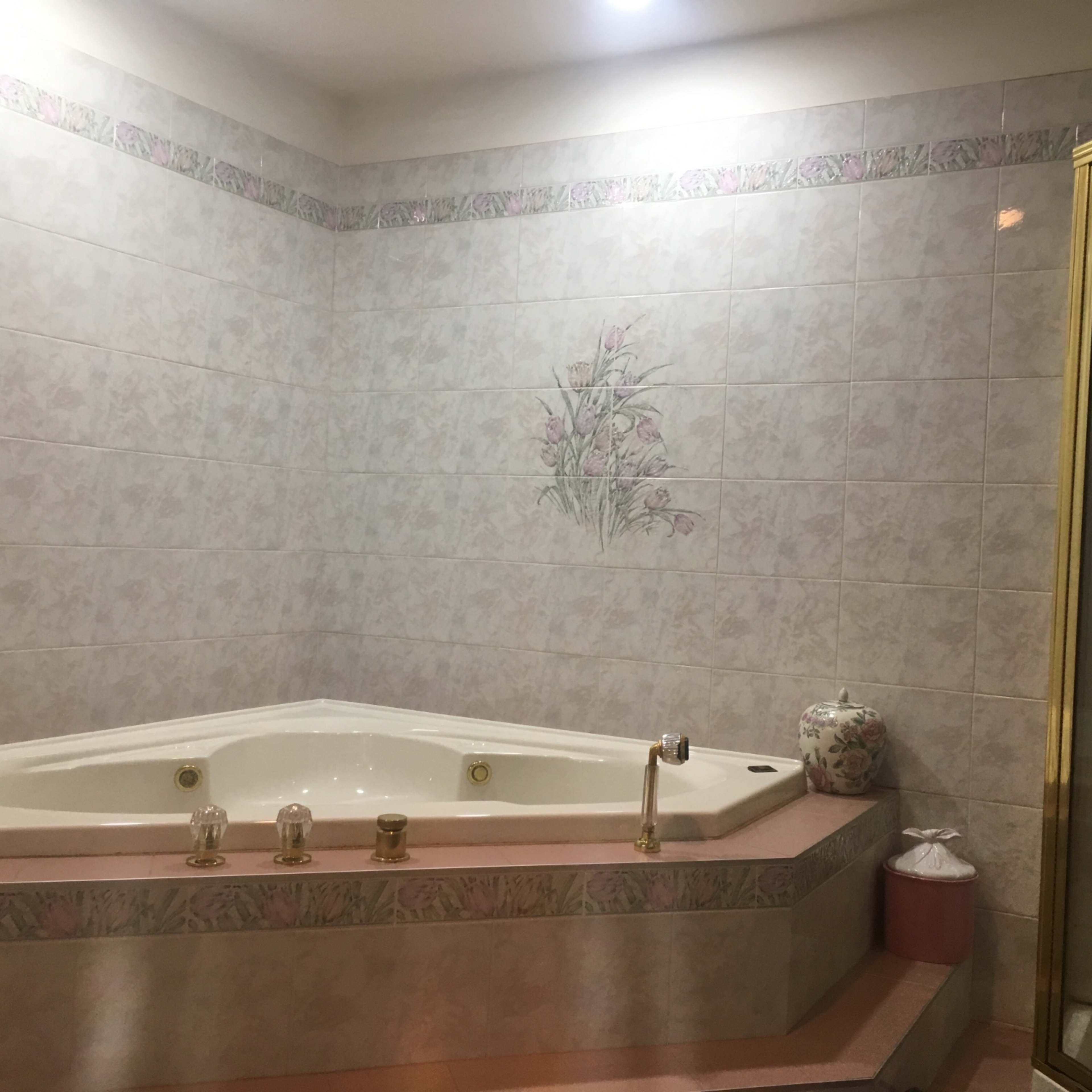 A corner bathtub with a floral design on the wall and a glass shower enclosure in a tiled bathroom.
