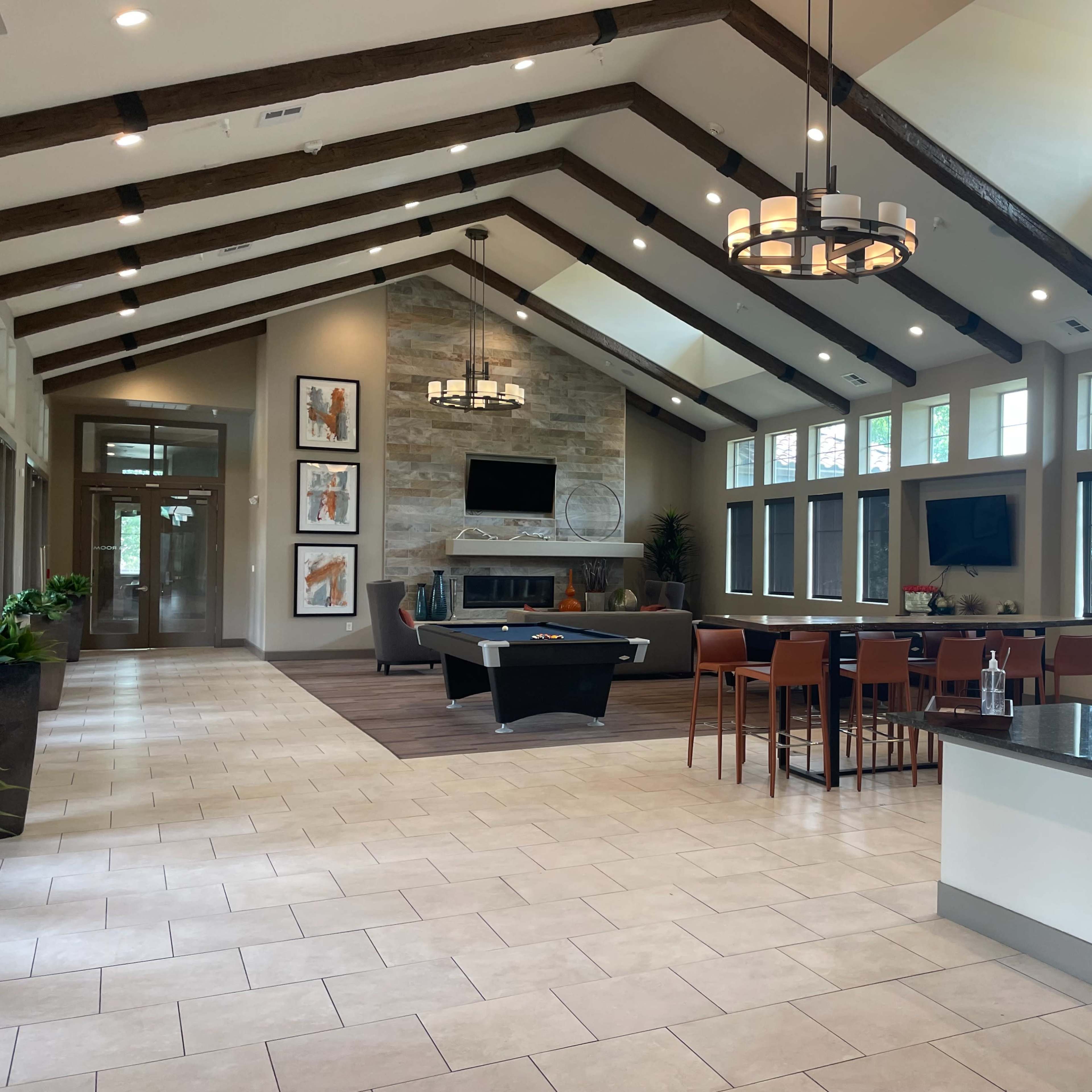 A spacious interior of a modern lounge area featuring a pool table, dining area, and large windows with natural light.