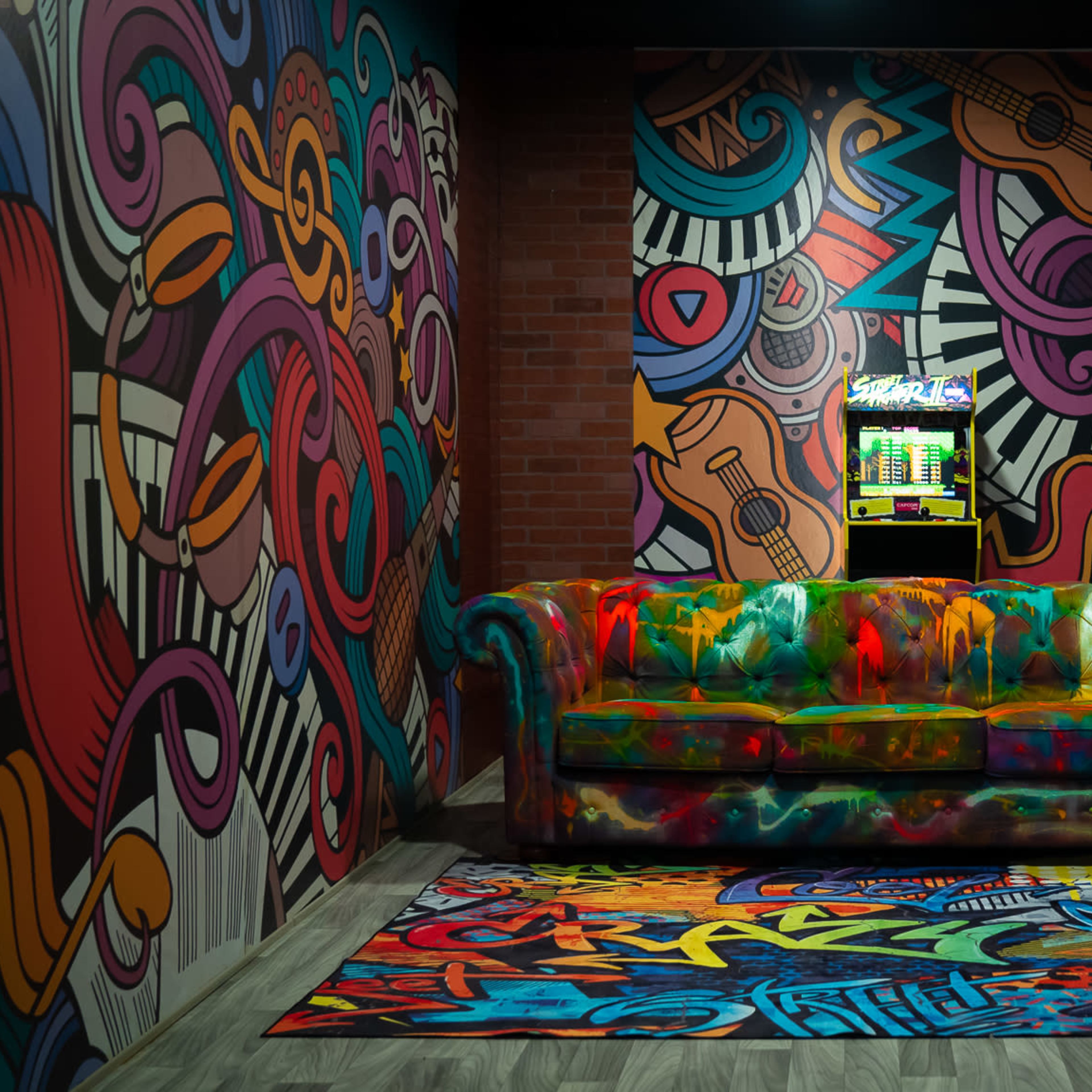 The scene features a vibrant, graffiti-covered room with a colorful couch and a patterned rug, all surrounded by eclectic wall art and a small arcade machine.
