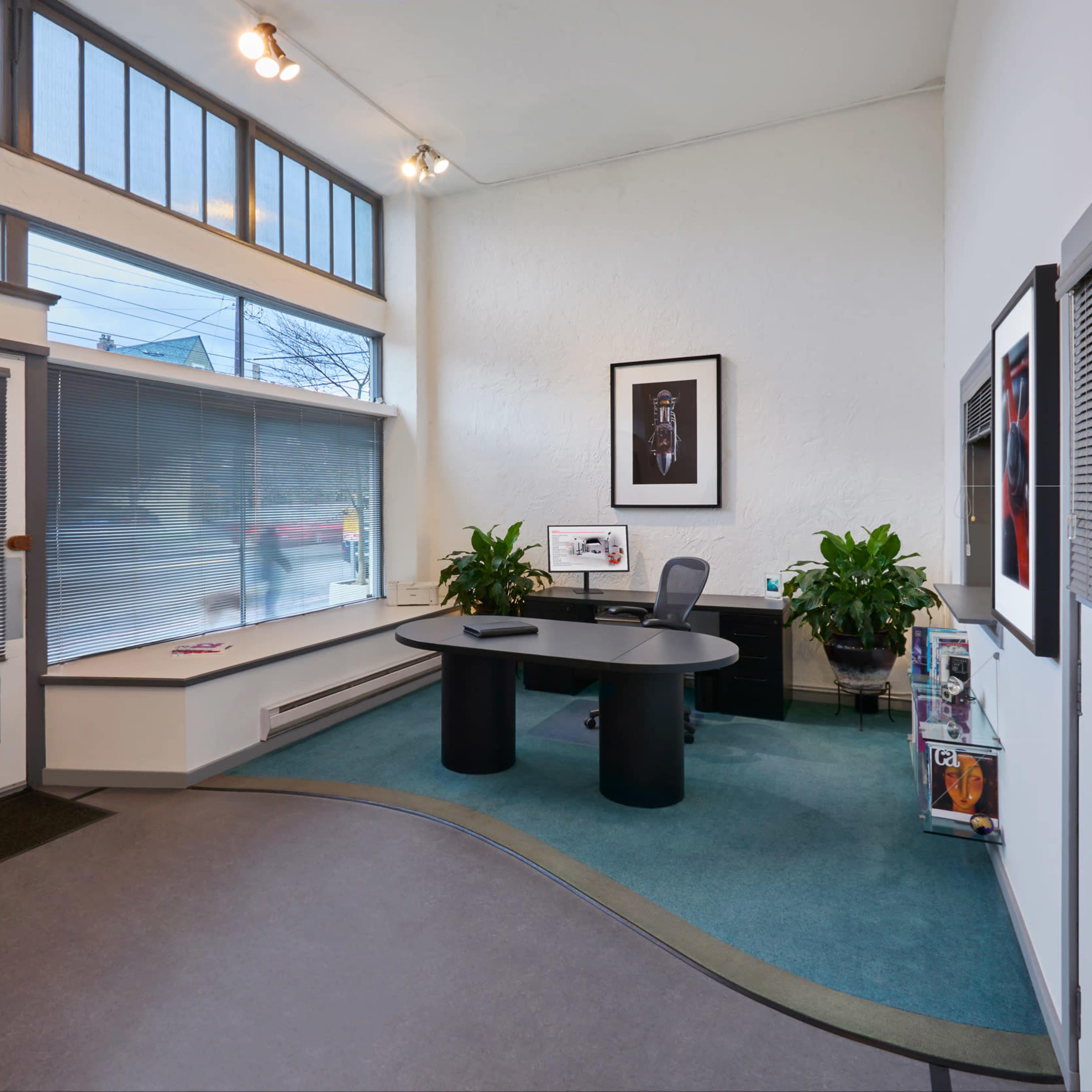 An office interior features a curved desk, large windows, and plants, creating a bright and spacious environment.
