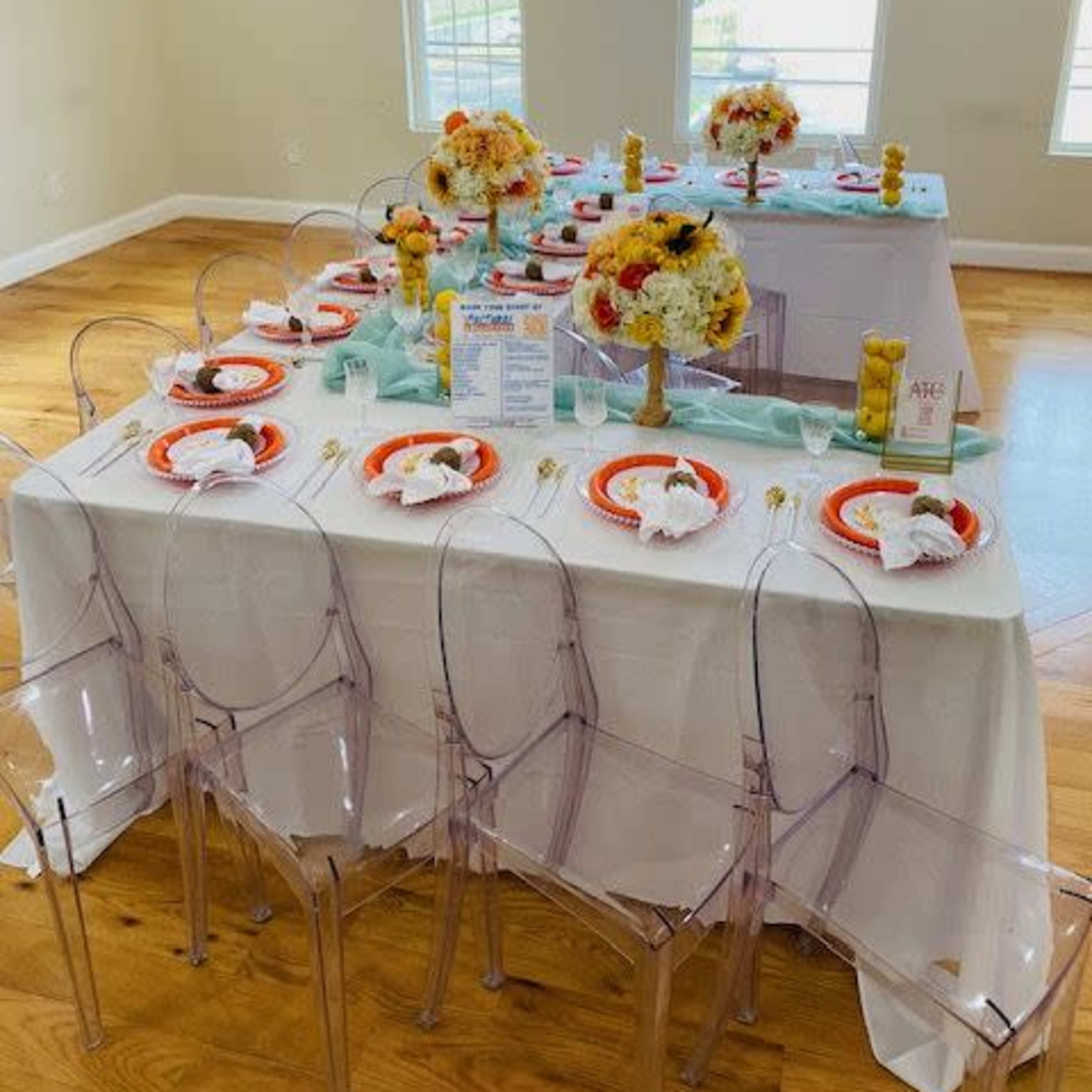 A neatly arranged dining table with colorful tableware and floral centerpieces is set in a well-lit room with large windows.