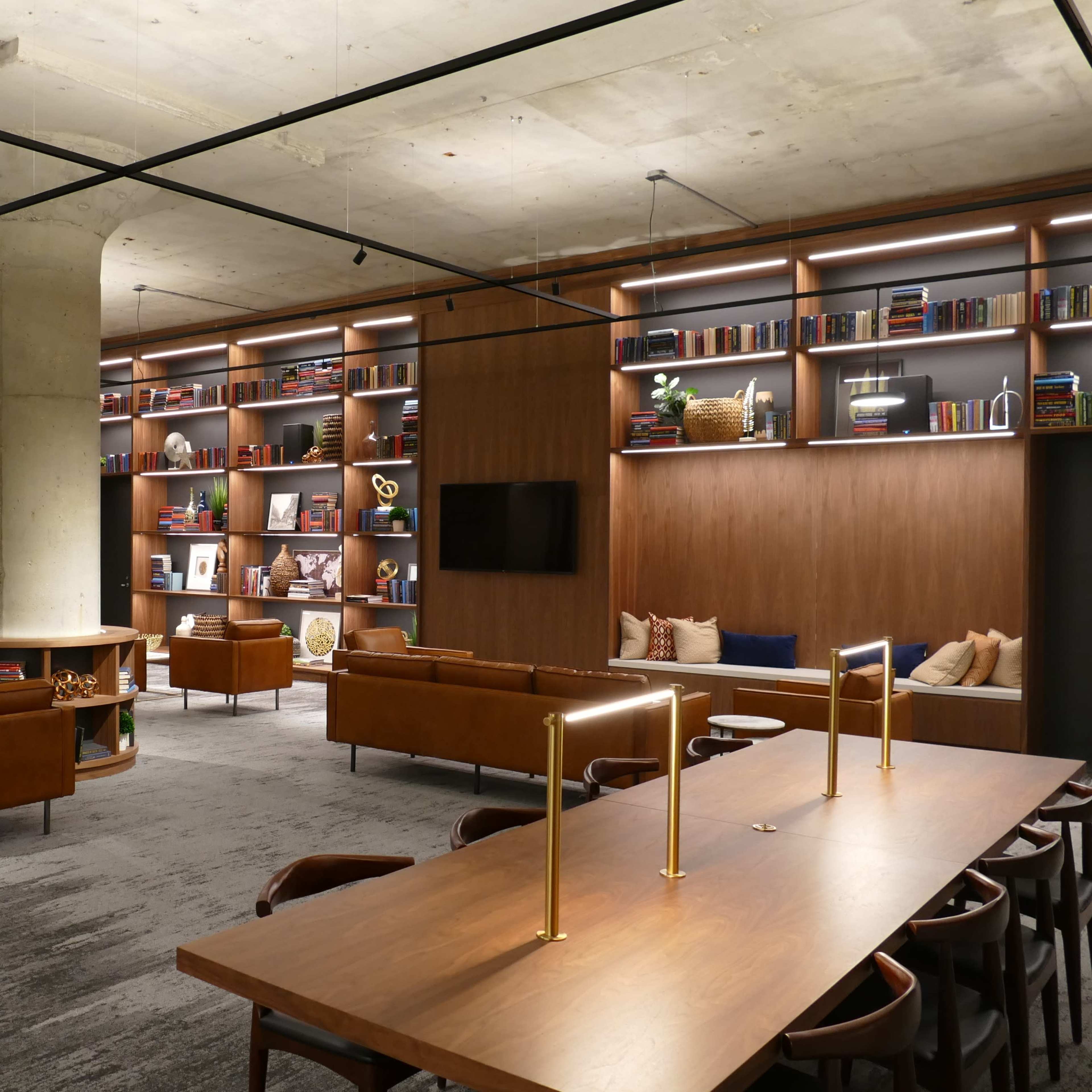 A modern lounge area with leather seating, wooden tables, and shelves filled with books.