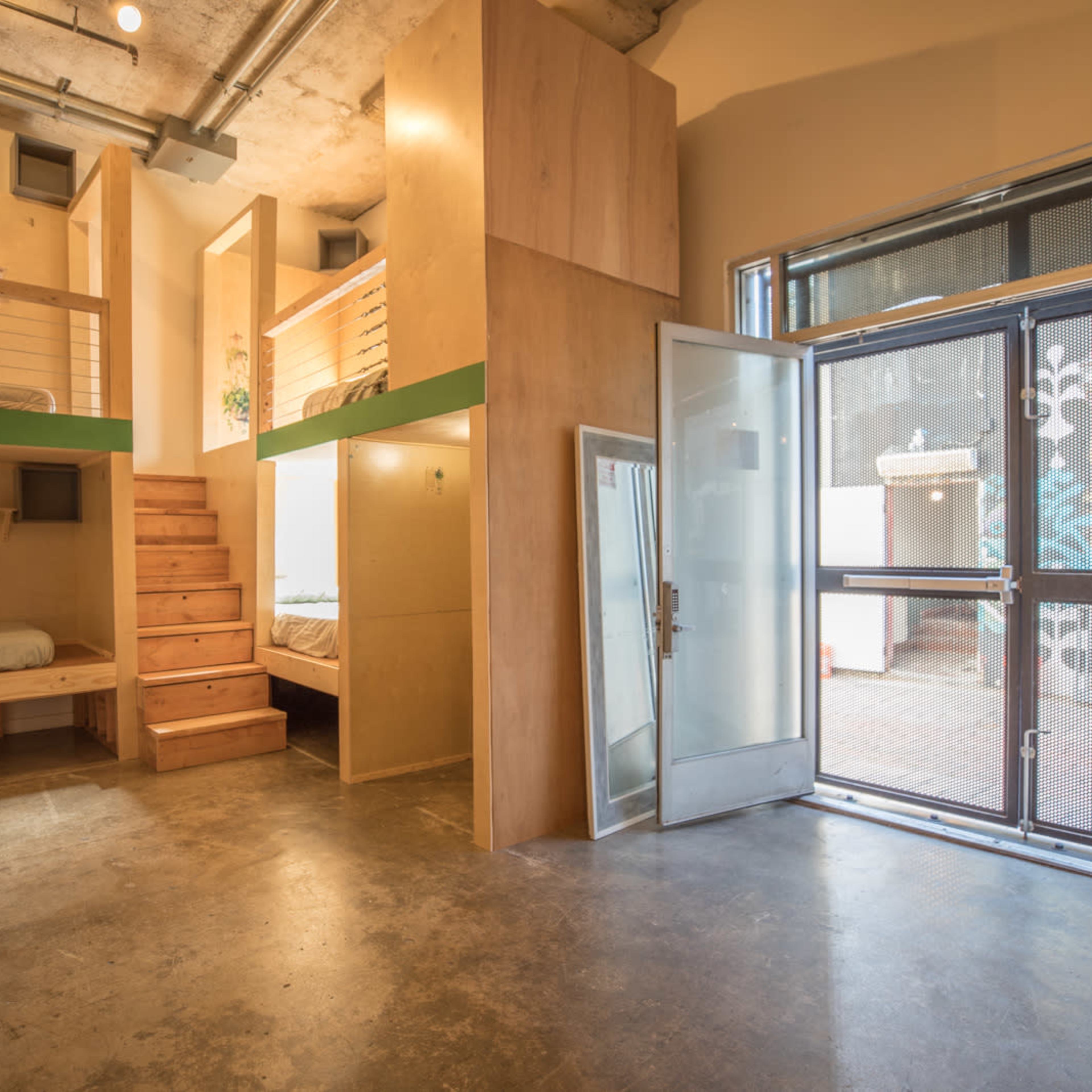 A modern interior space featuring two elevated sleeping areas, wooden steps leading to one of the beds, and a large glass door that opens to the outside.