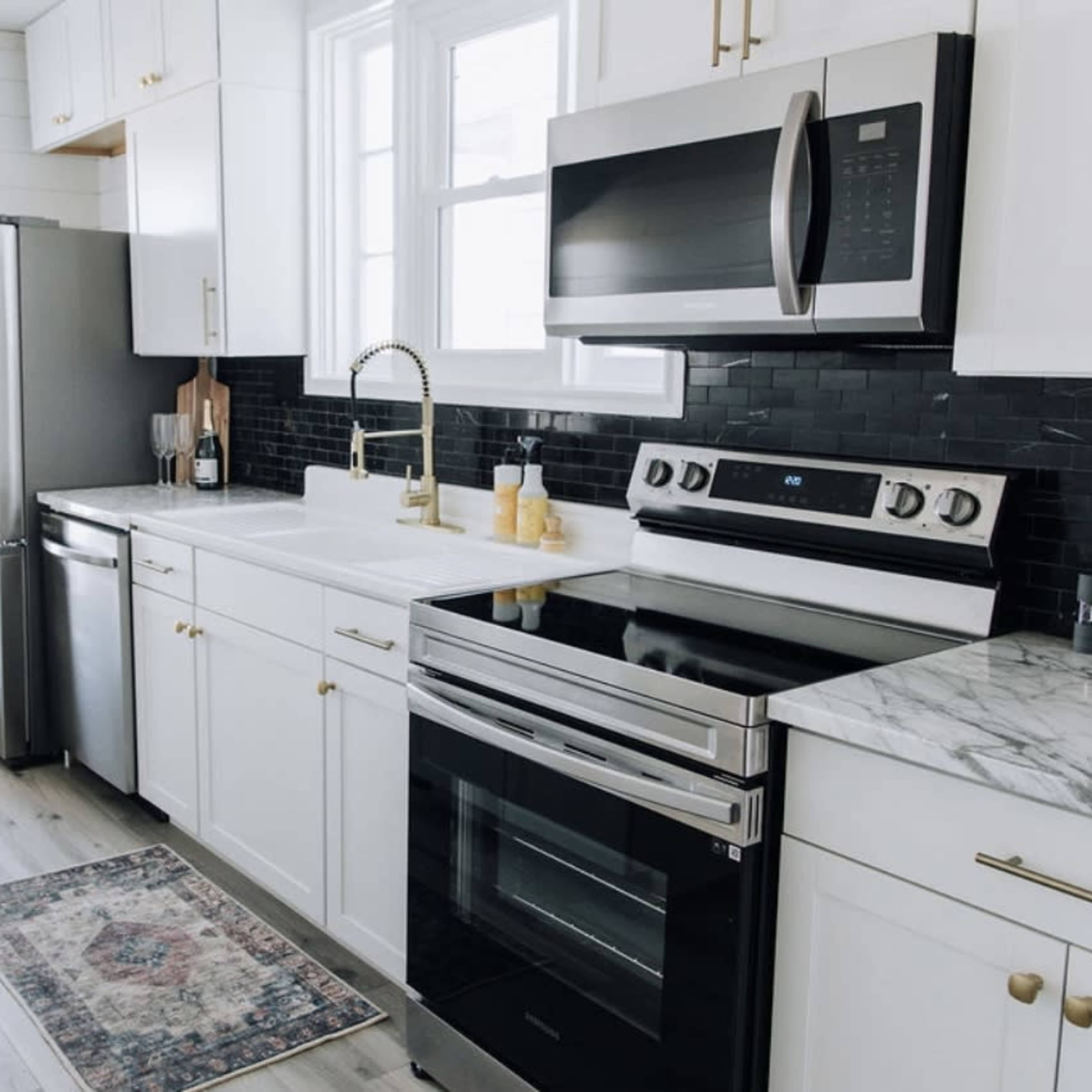 A modern kitchen features white cabinetry, stainless steel appliances, a marble countertop, and a patterned rug on the floor.