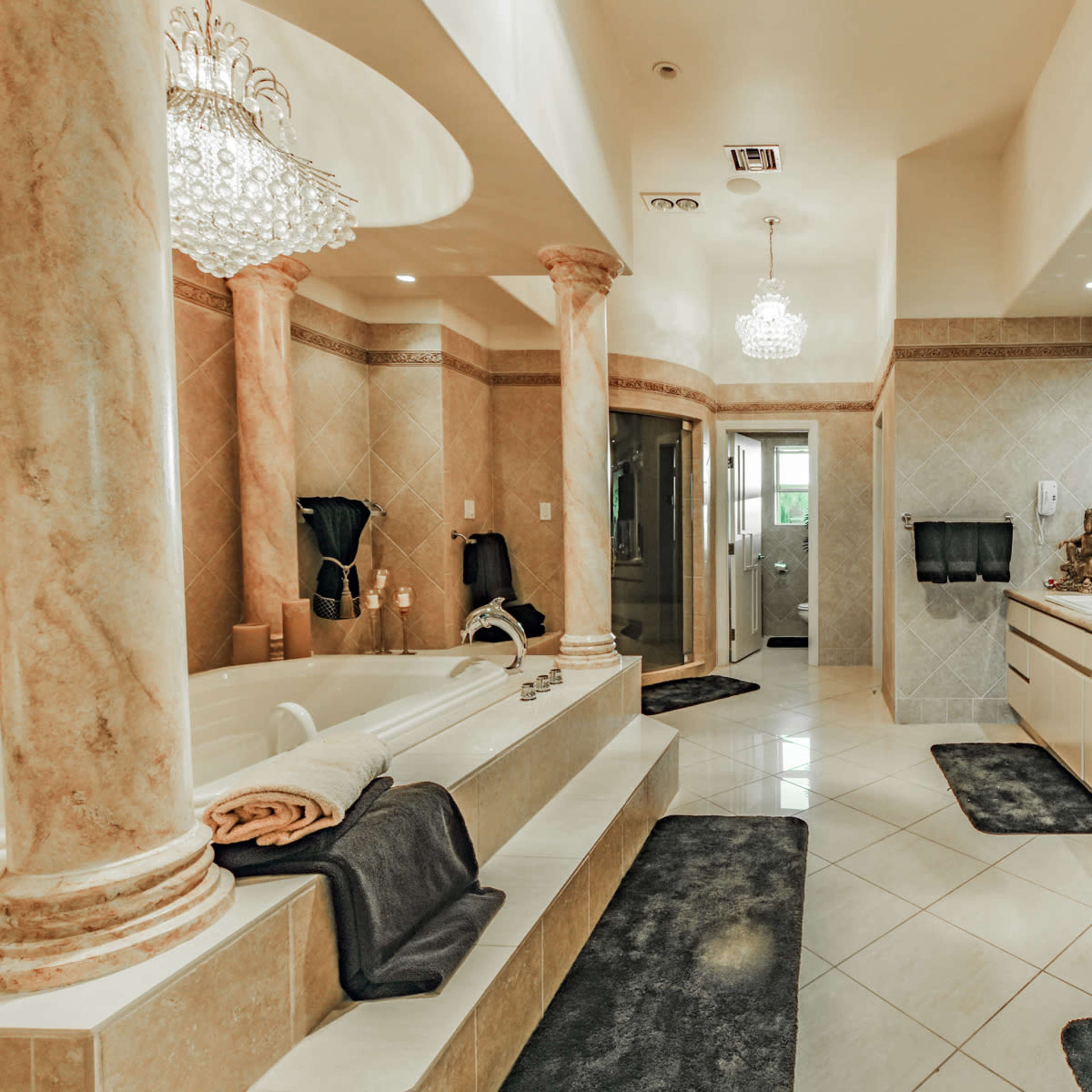 A spacious bathroom featuring marble columns, a large soaking tub, and a double vanity with decorative accents.