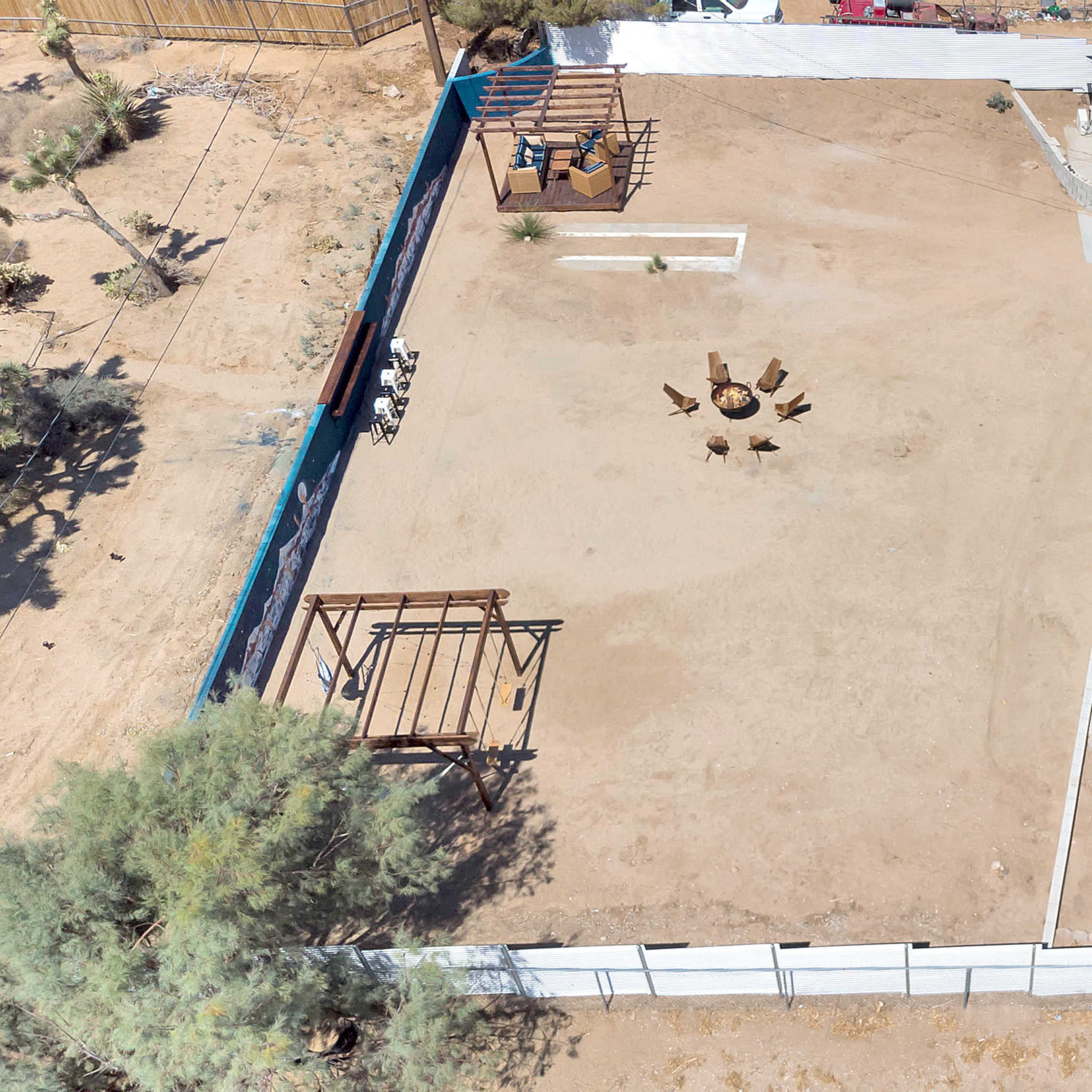 A residential property with a large, empty yard featuring a fire pit in the center, surrounded by a fence, and a house with a black roof on one side.
