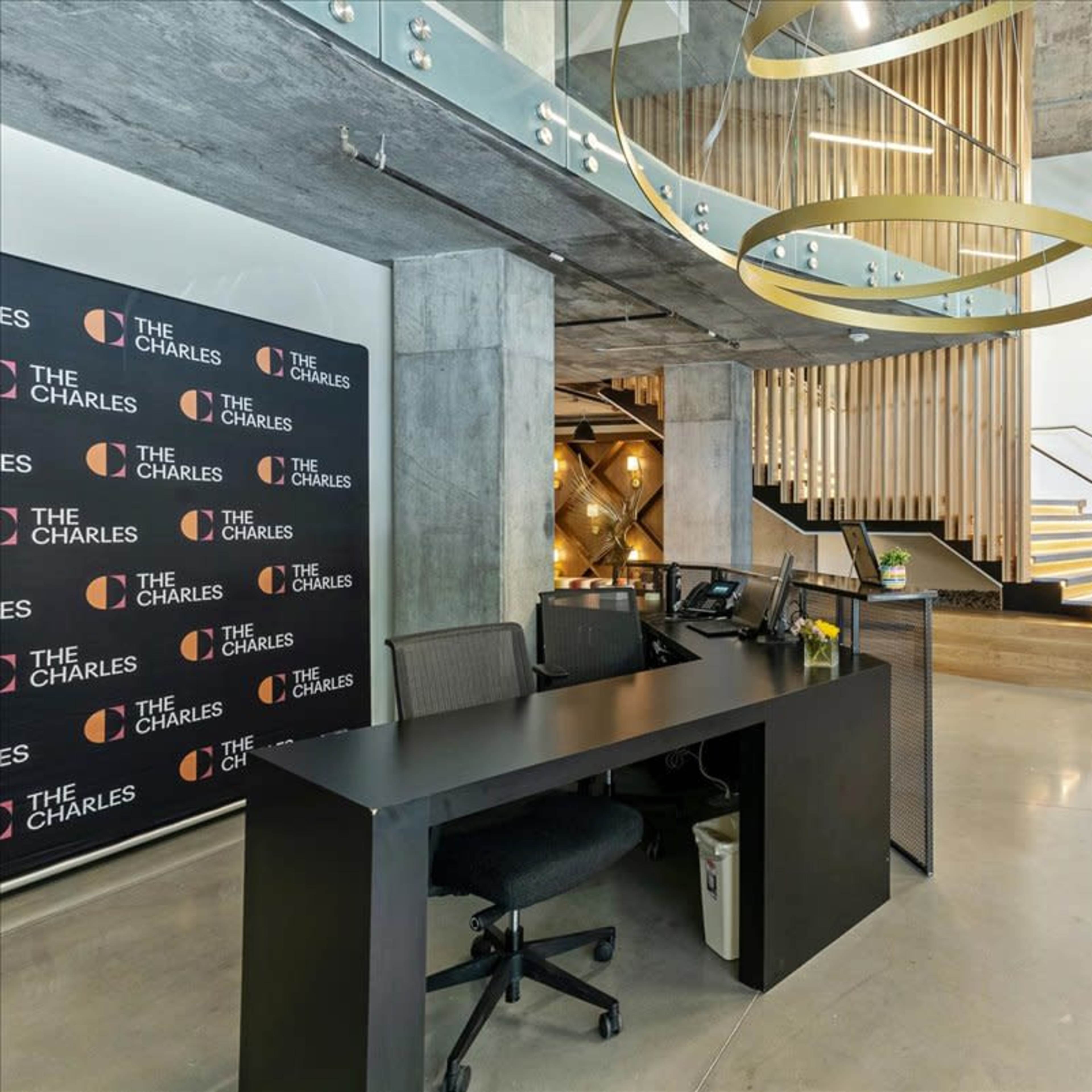 A modern reception area with a desk, decorative wood panels, a staircase, and a wall featuring the logo "The Charles."