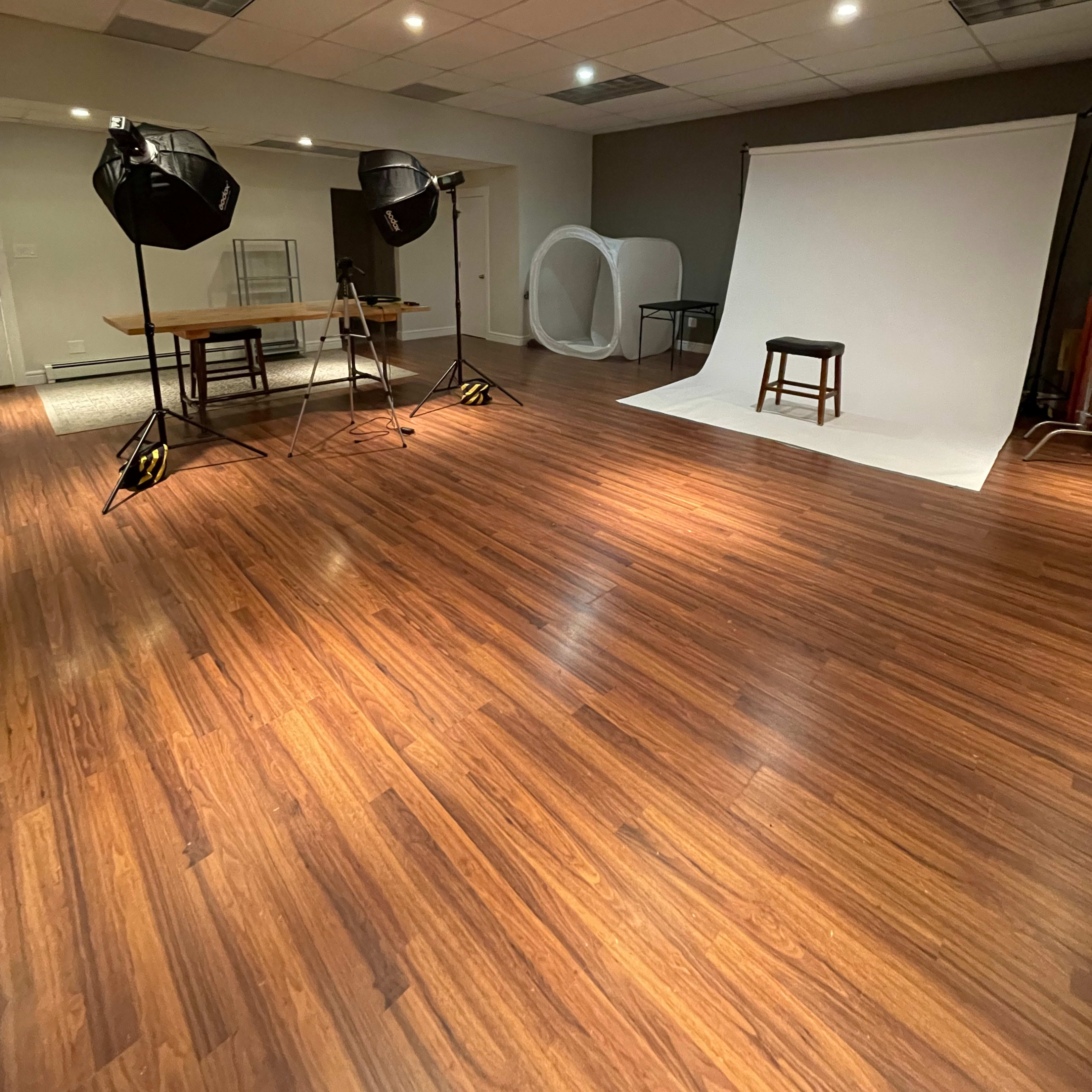 A photography studio with a white backdrop, a stool, and two studio lights positioned on tripods.