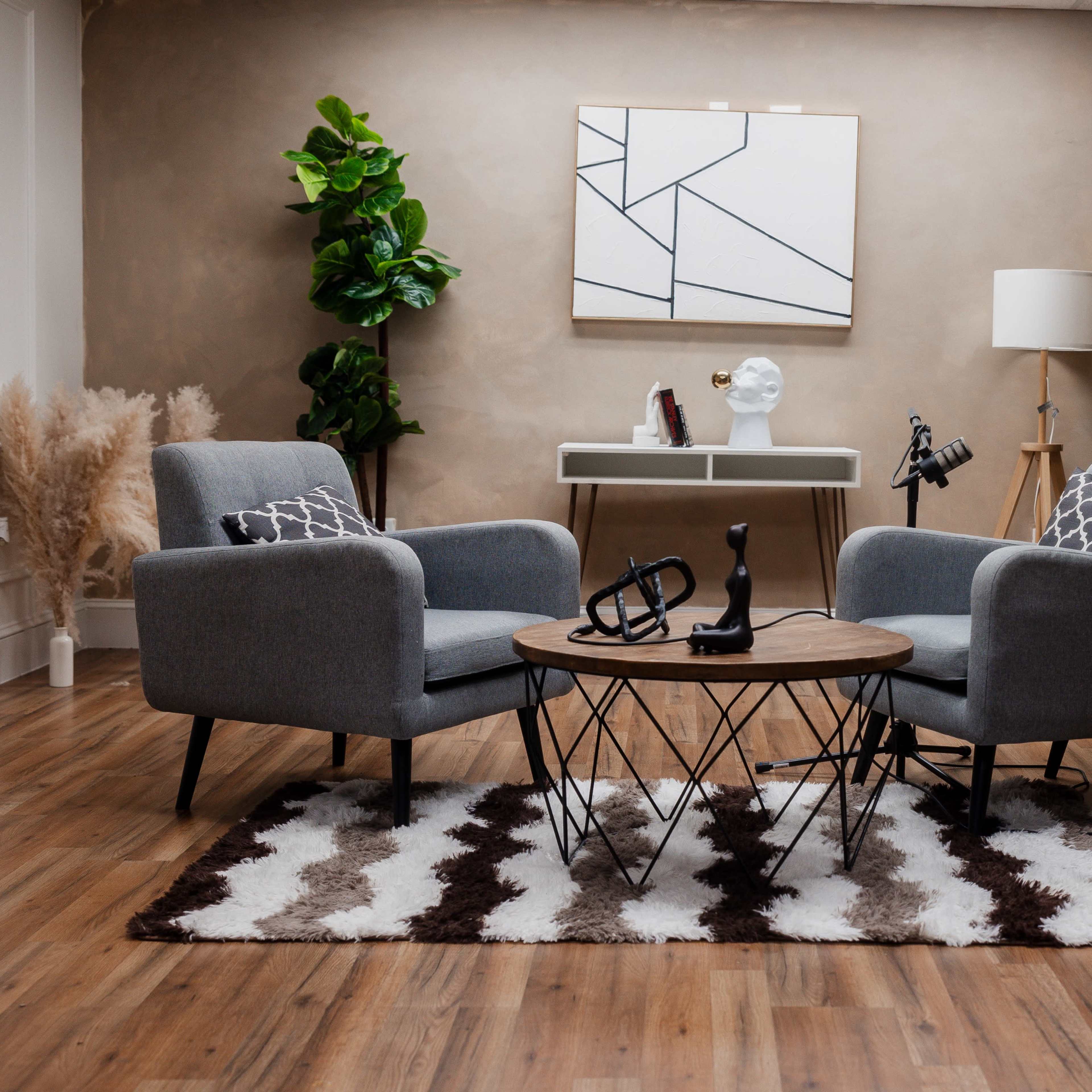 A contemporary living room setup featuring two gray armchairs, a round coffee table, and decorative plants against a neutral wall.