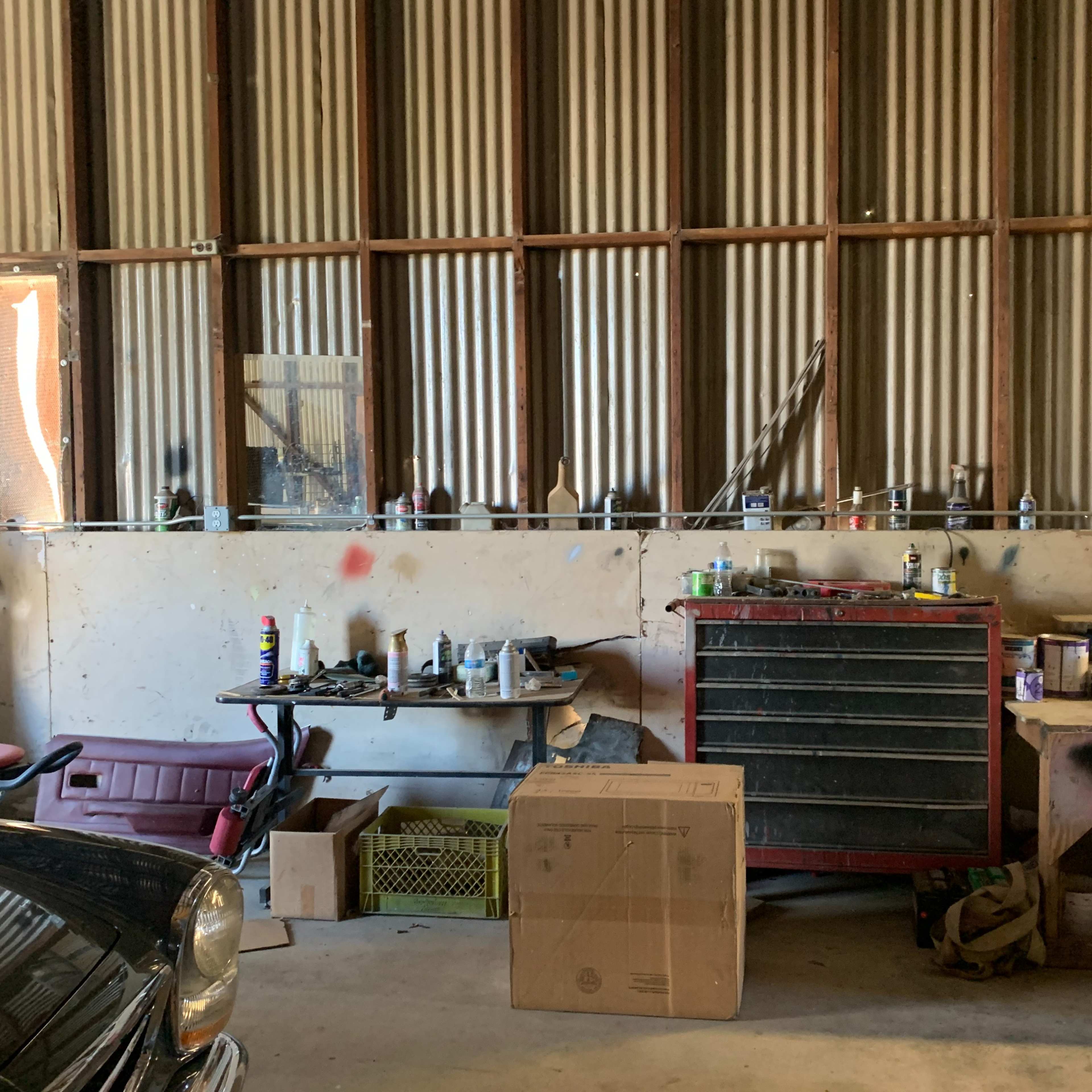 A shirtless man works on a classic car inside a dimly lit garage filled with various vehicles and tools.