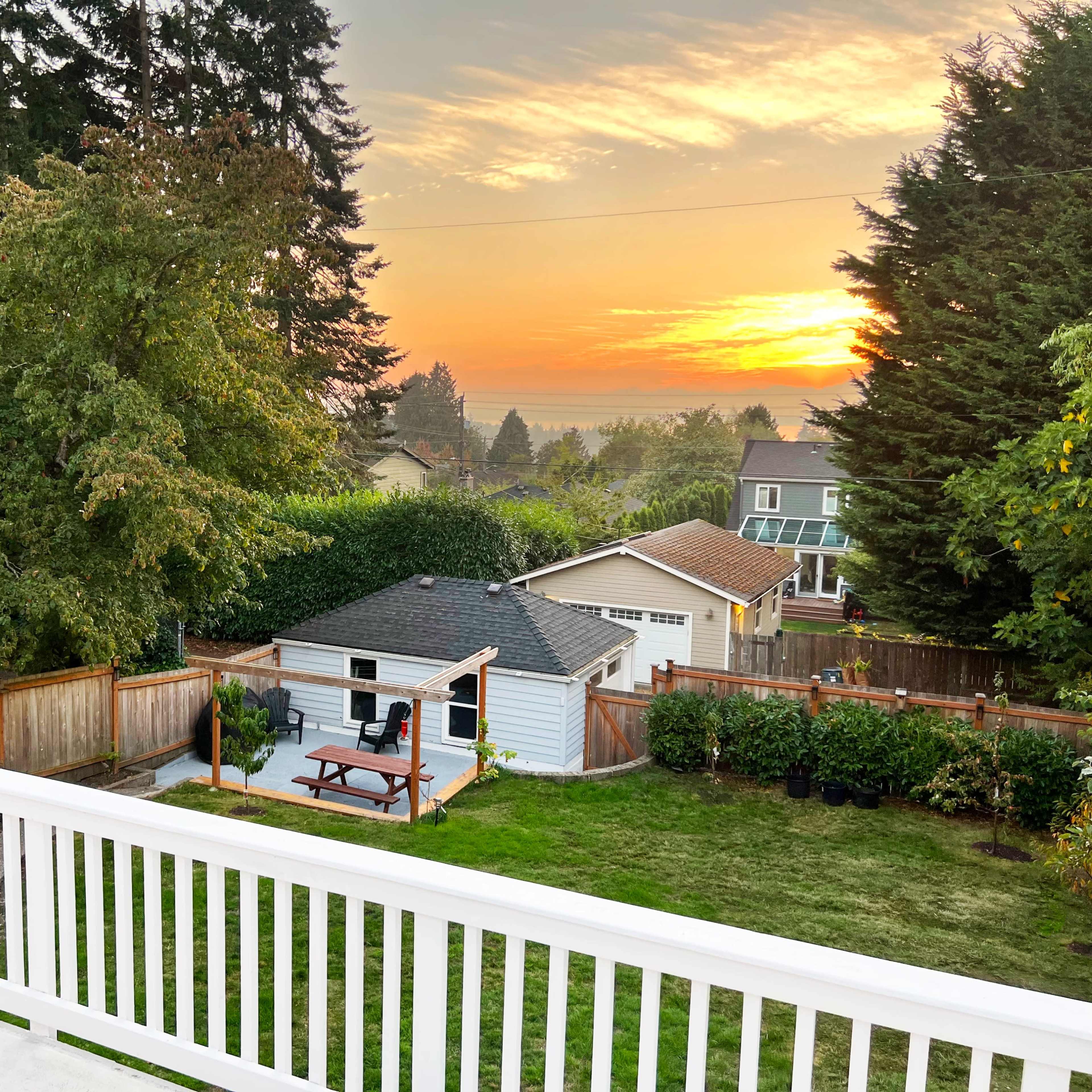 A backyard with a picnic table and a shed, framed by trees, as the sun sets in the background.