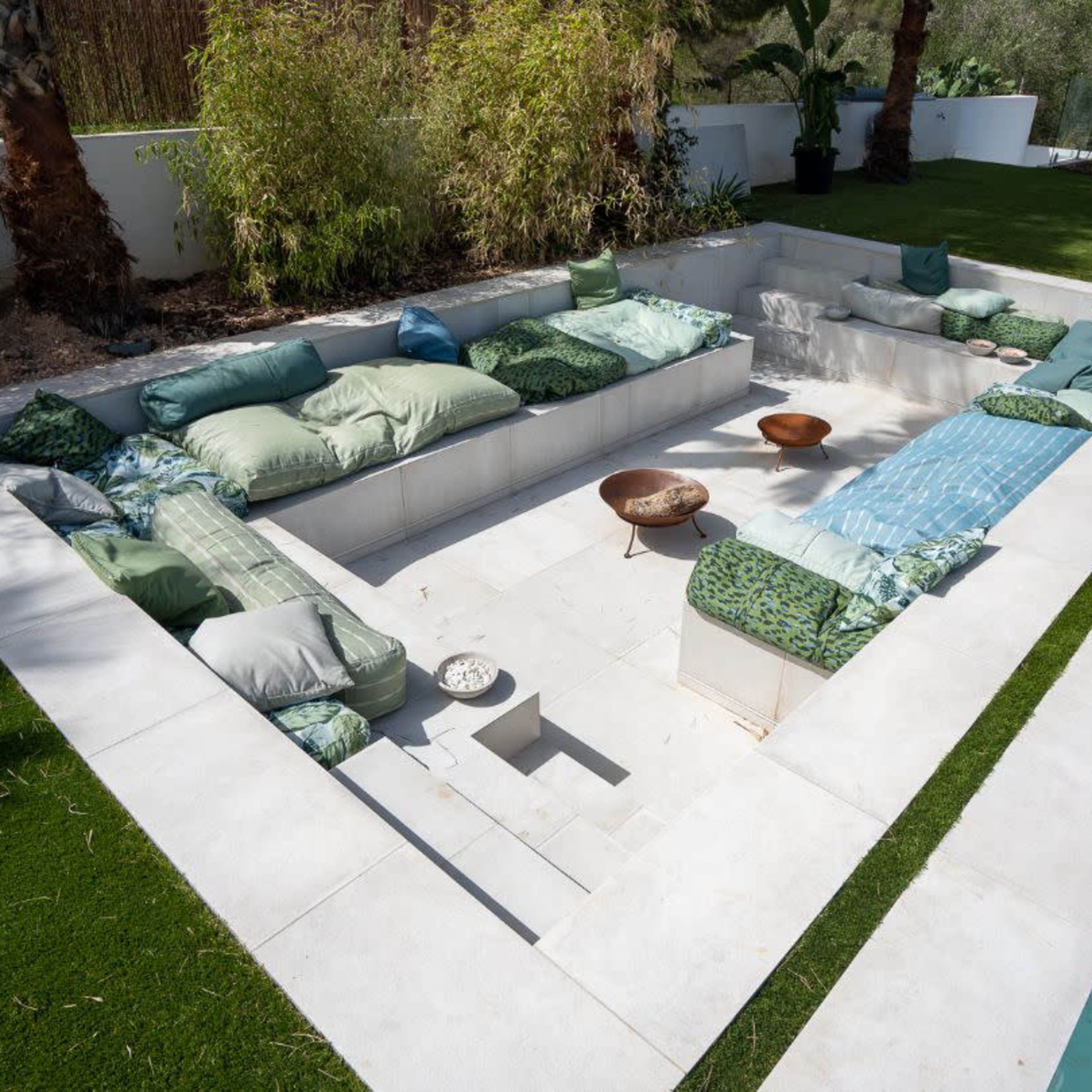 A modern outdoor seating area arranged in a sunken design, surrounded by lush greenery and adjacent to a swimming pool.