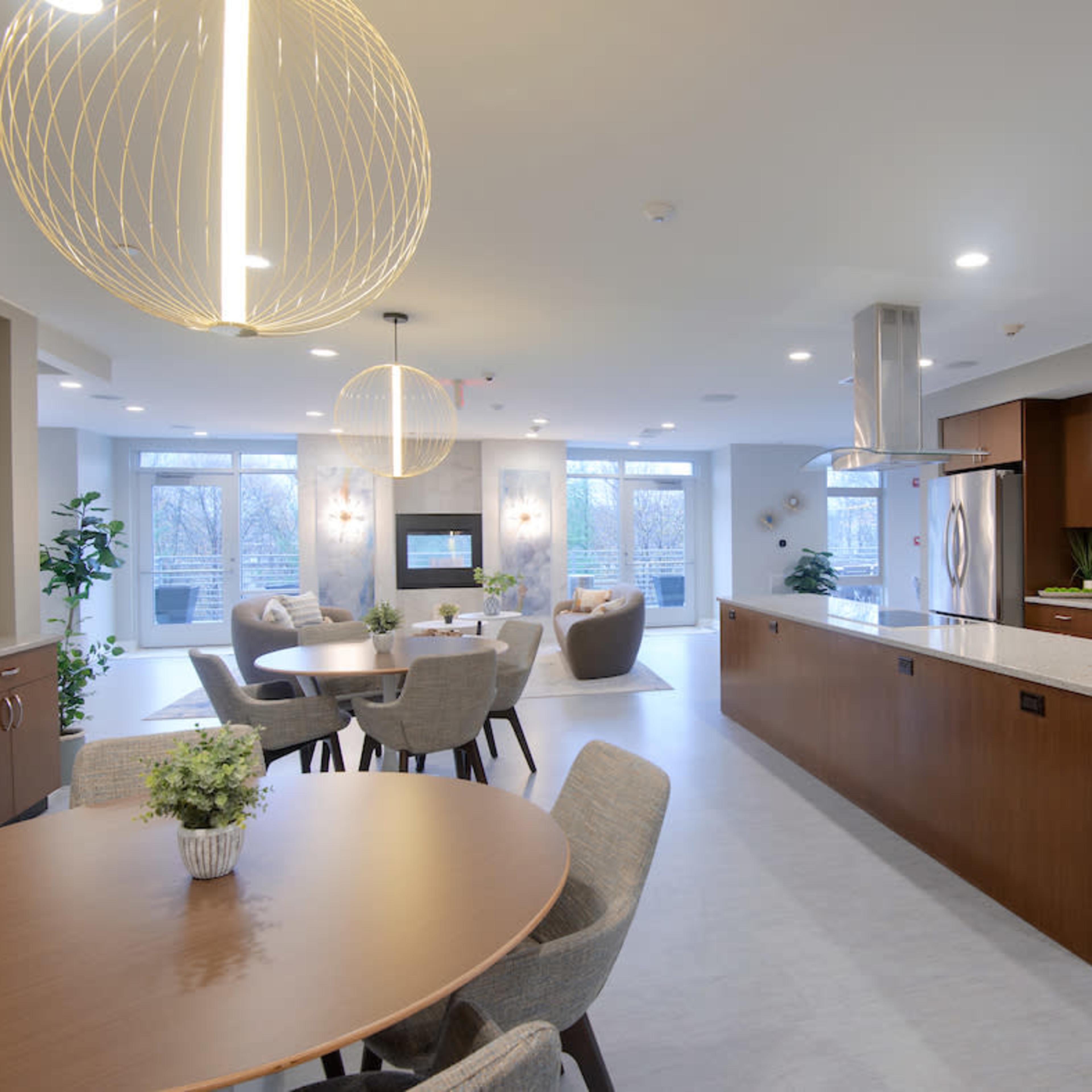 A modern kitchen and dining area features a long countertop, circular tables, and large windows overlooking an outdoor space.