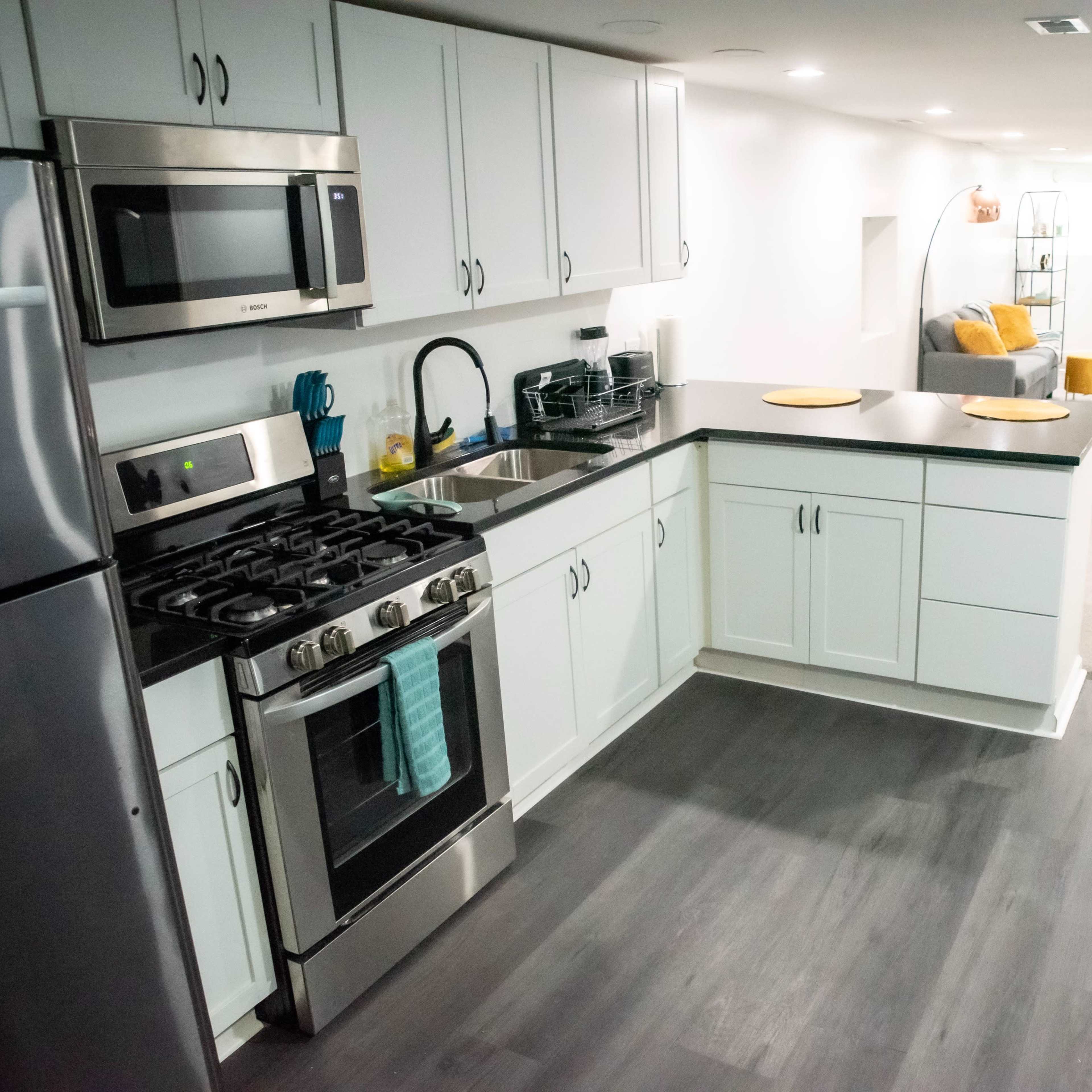 A modern kitchen area with stainless steel appliances, including a gas stove, alongside a dining space featuring a gray sofa in a well-lit corridor.