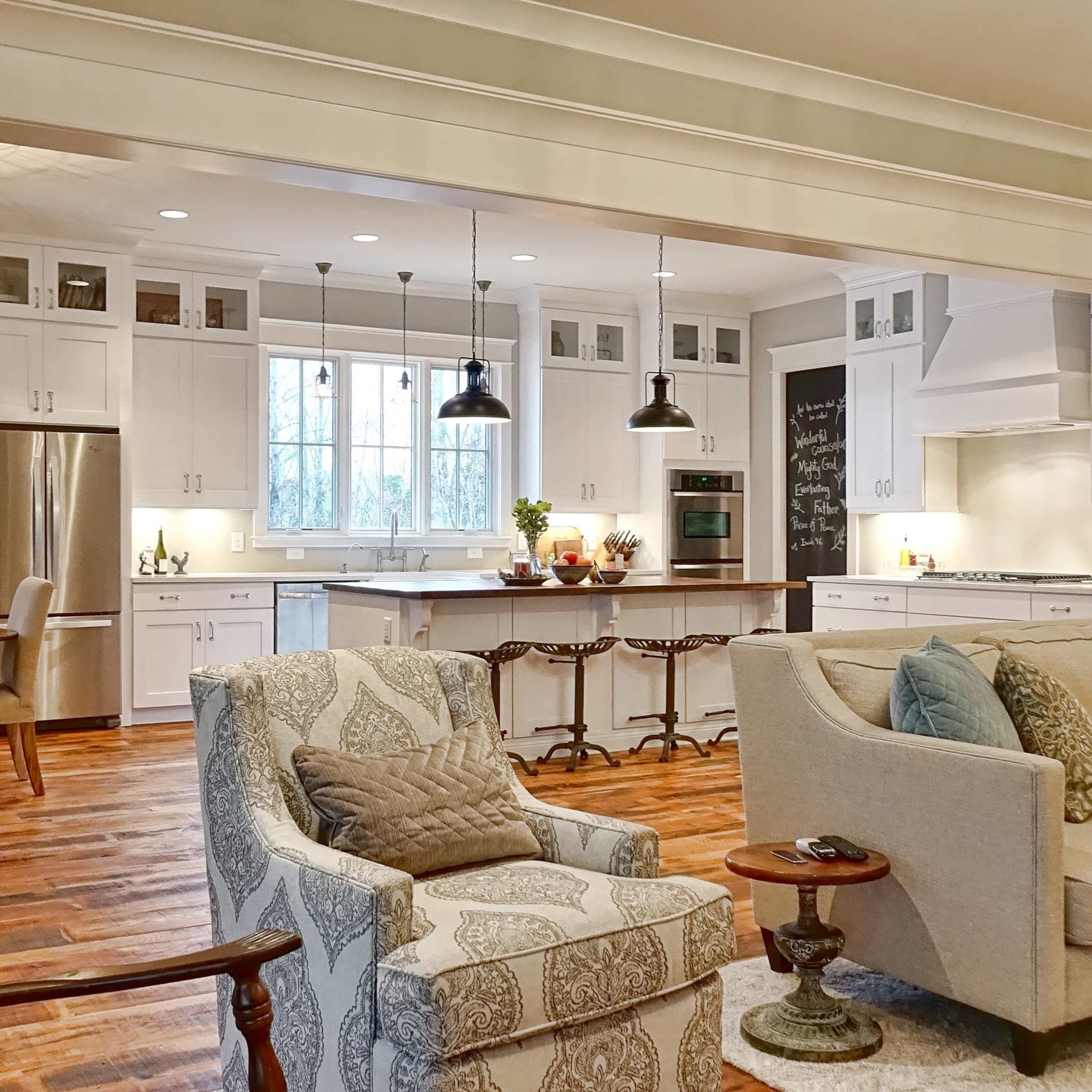 A spacious kitchen and living area featuring white cabinetry, a wooden floor, and a large island with bar stools.